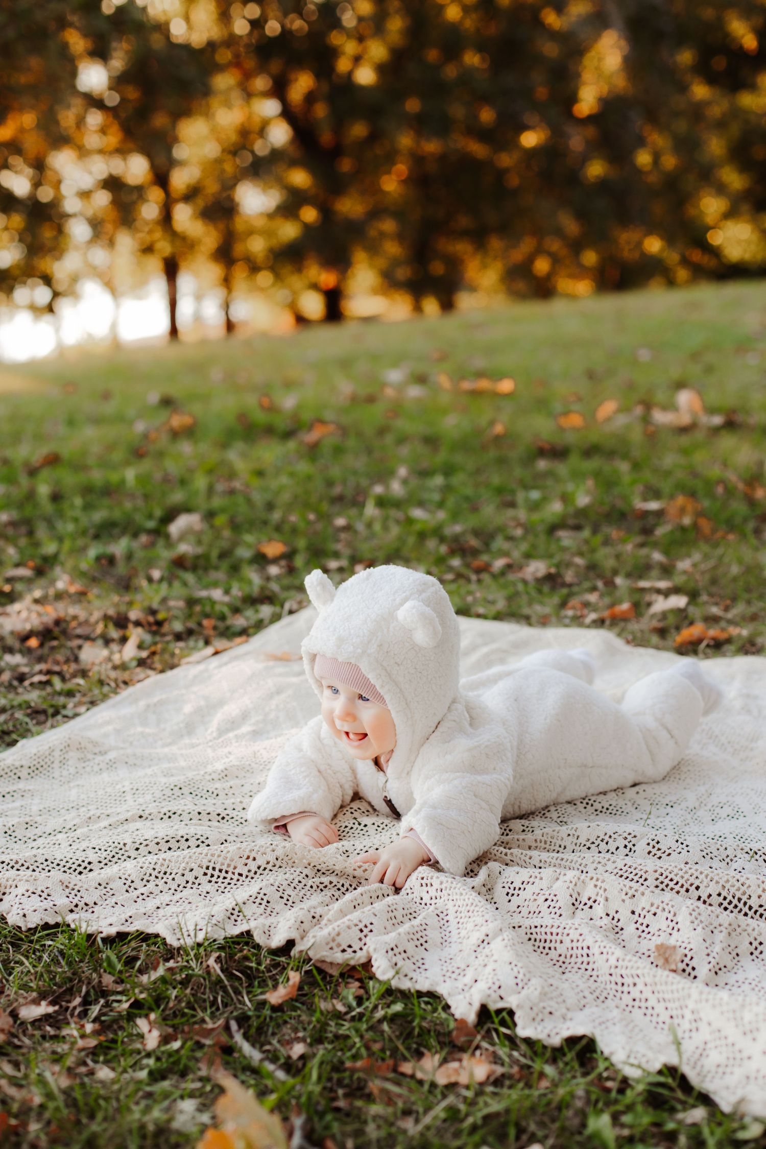Baby lying on white lace blanket surrounded by autumn leaves.