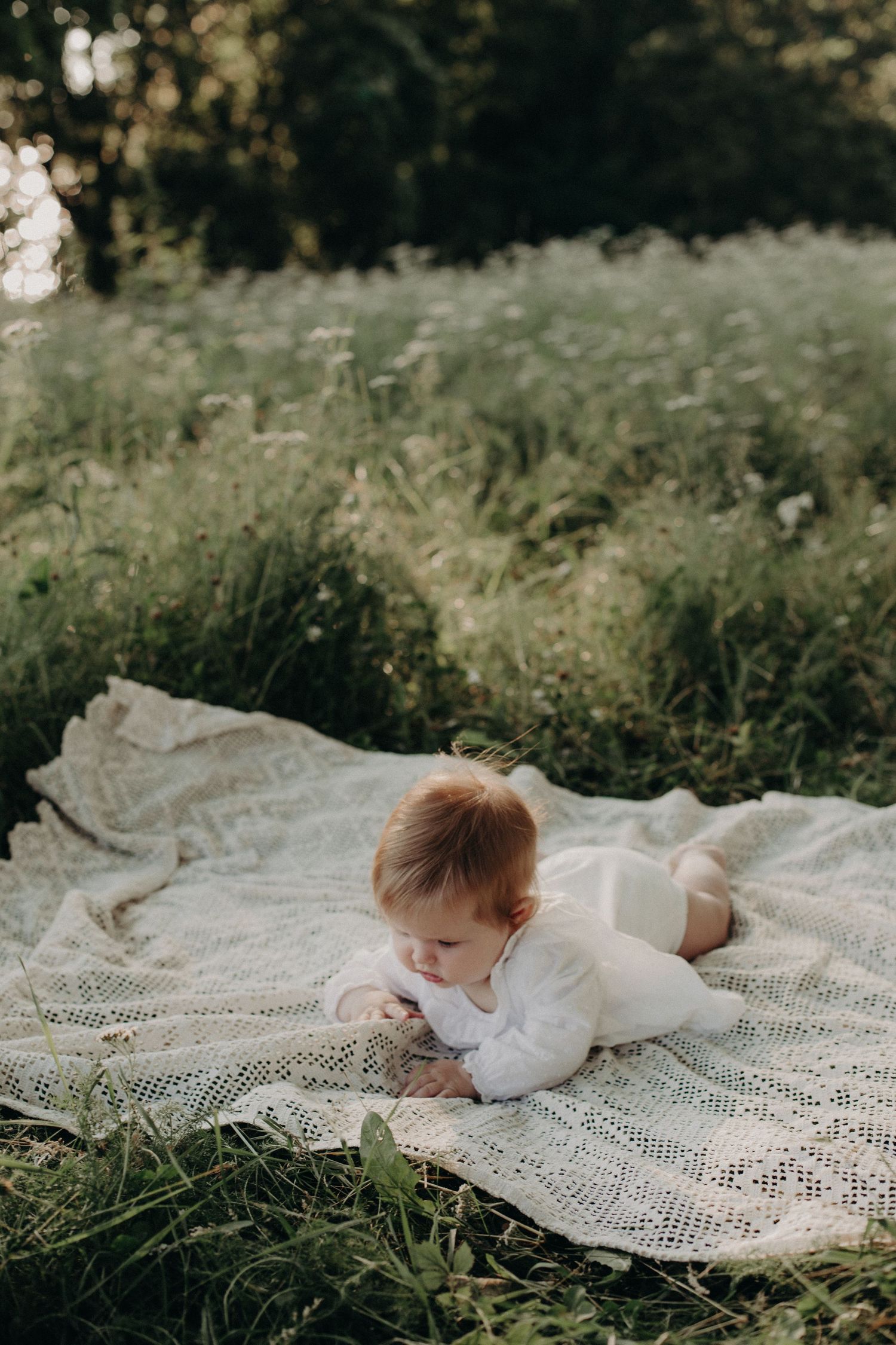 Child lying on lace blanket in grassy outdoor setting.