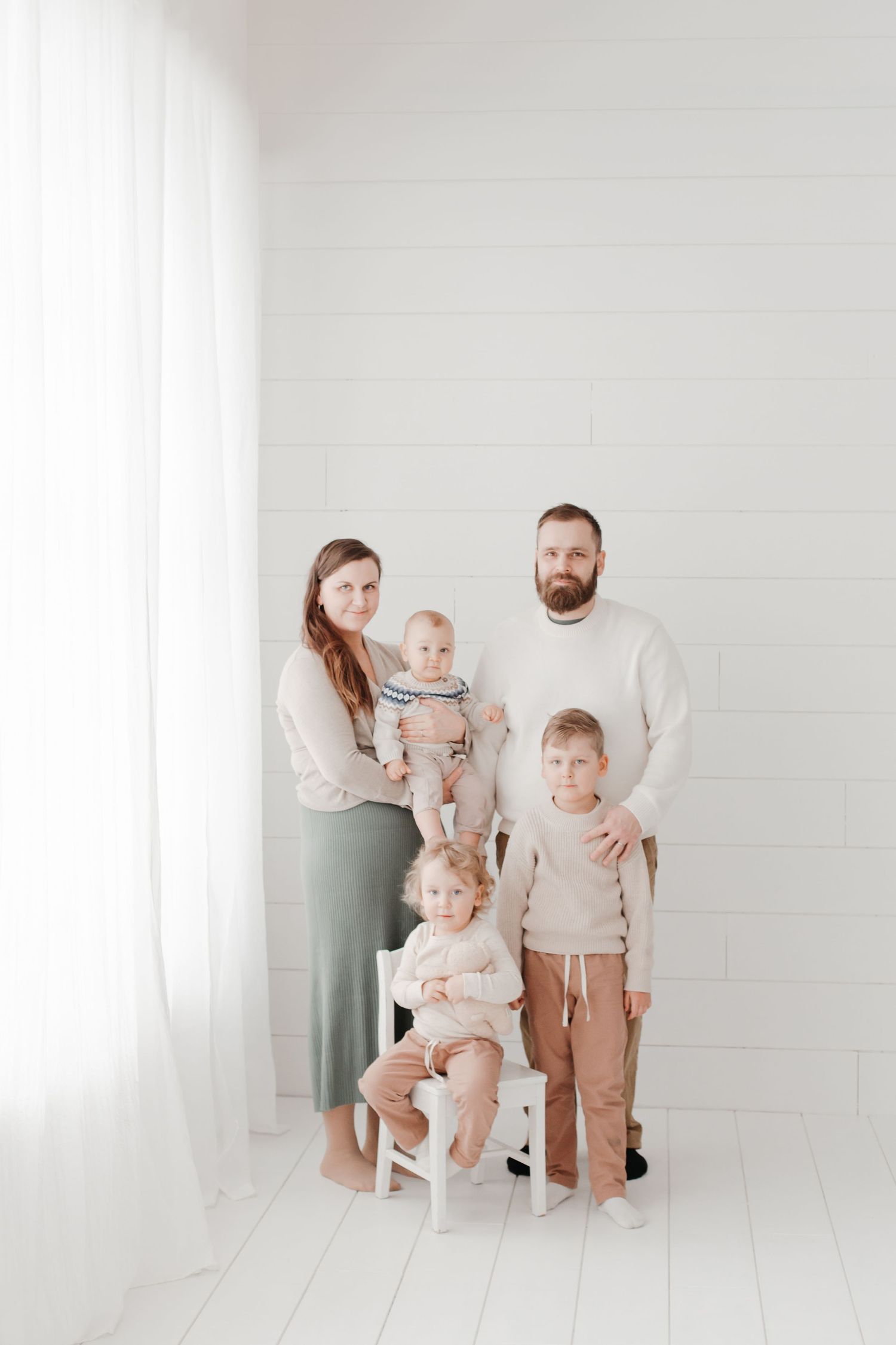 Family in coordinated neutral outfits poses playfully in a bright white studio setting.