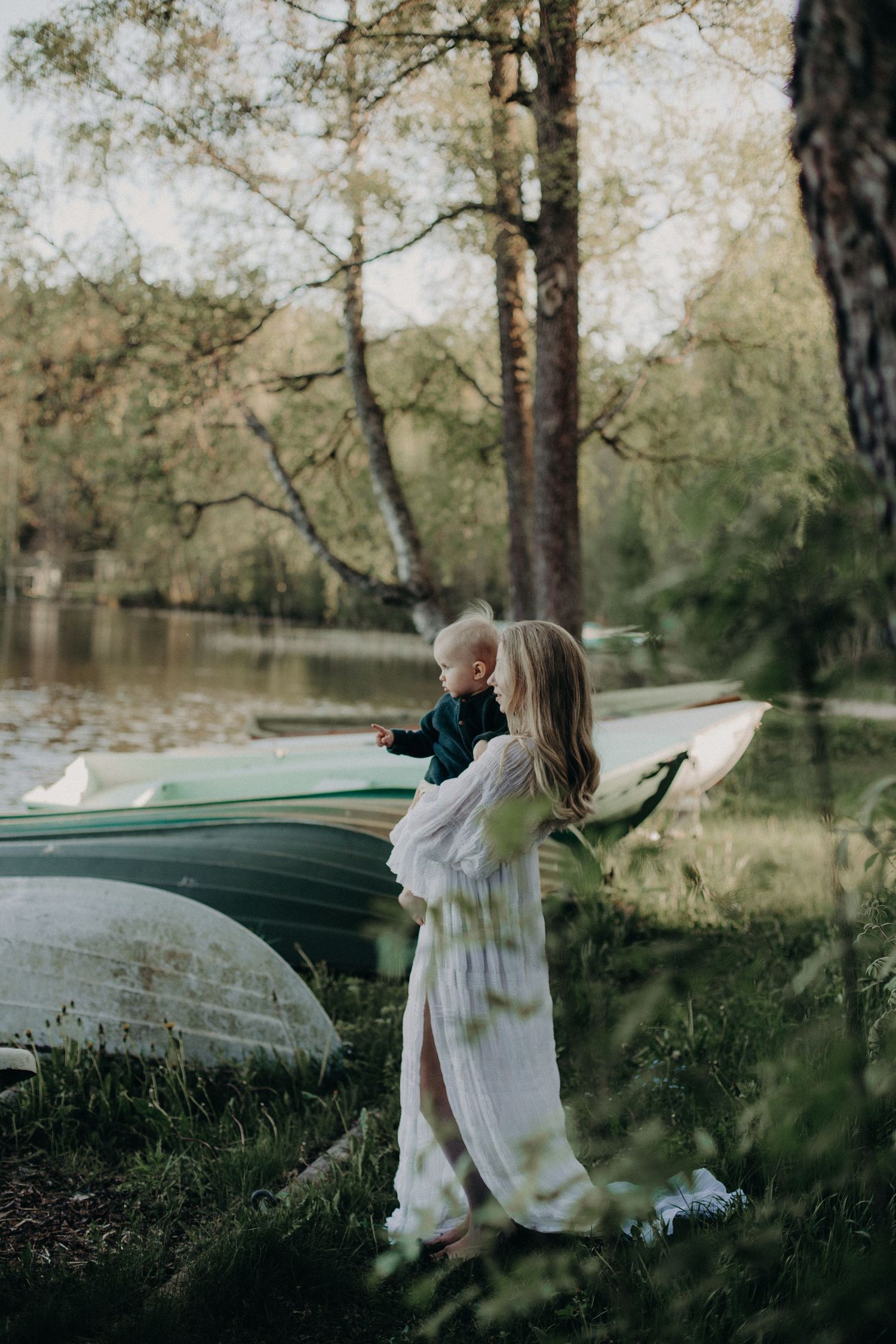 Dreamy scene by a lake with overturned boats and figure in flowing white dress.