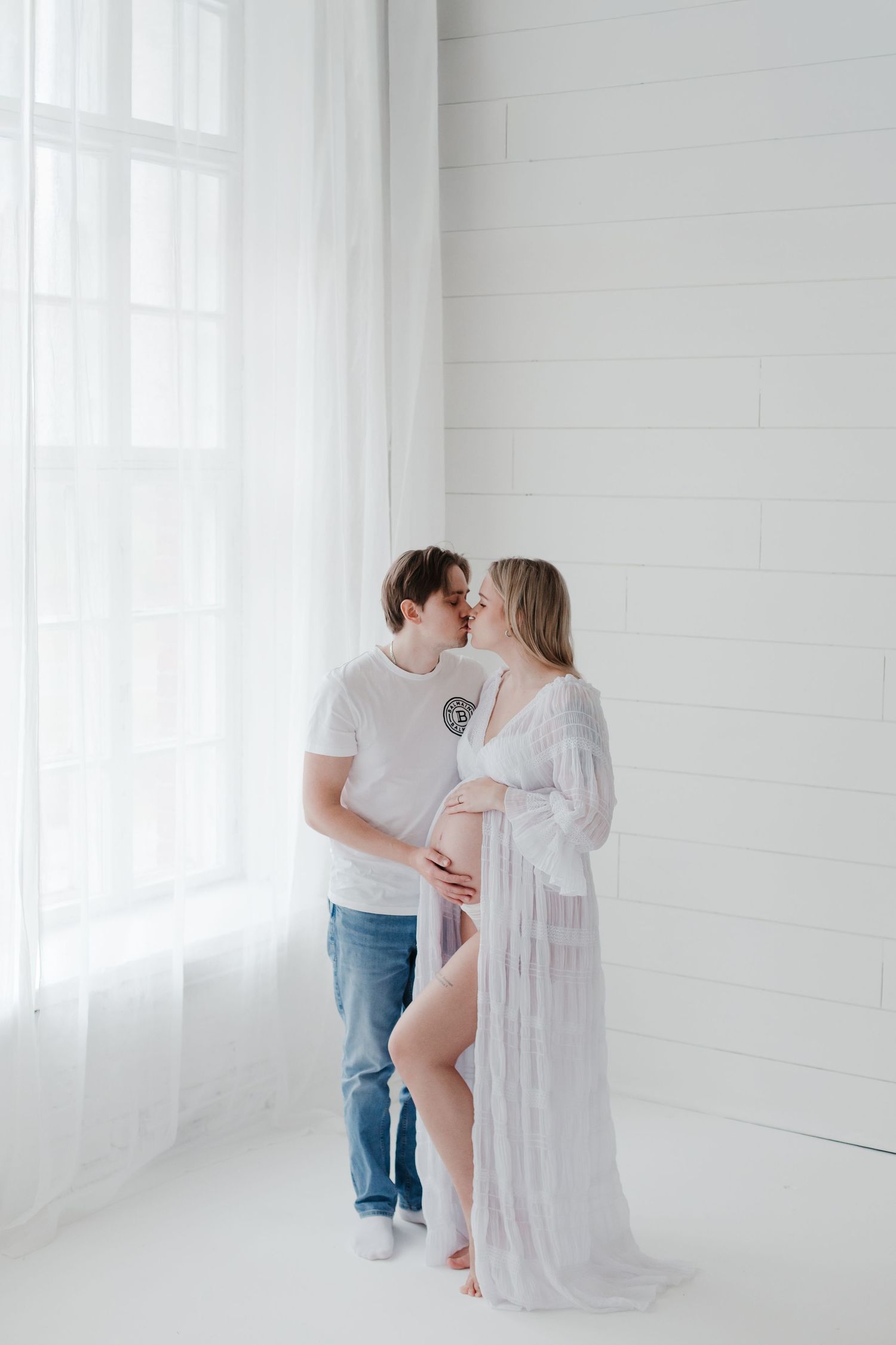 Tender maternity moment captured in bright white studio setting.