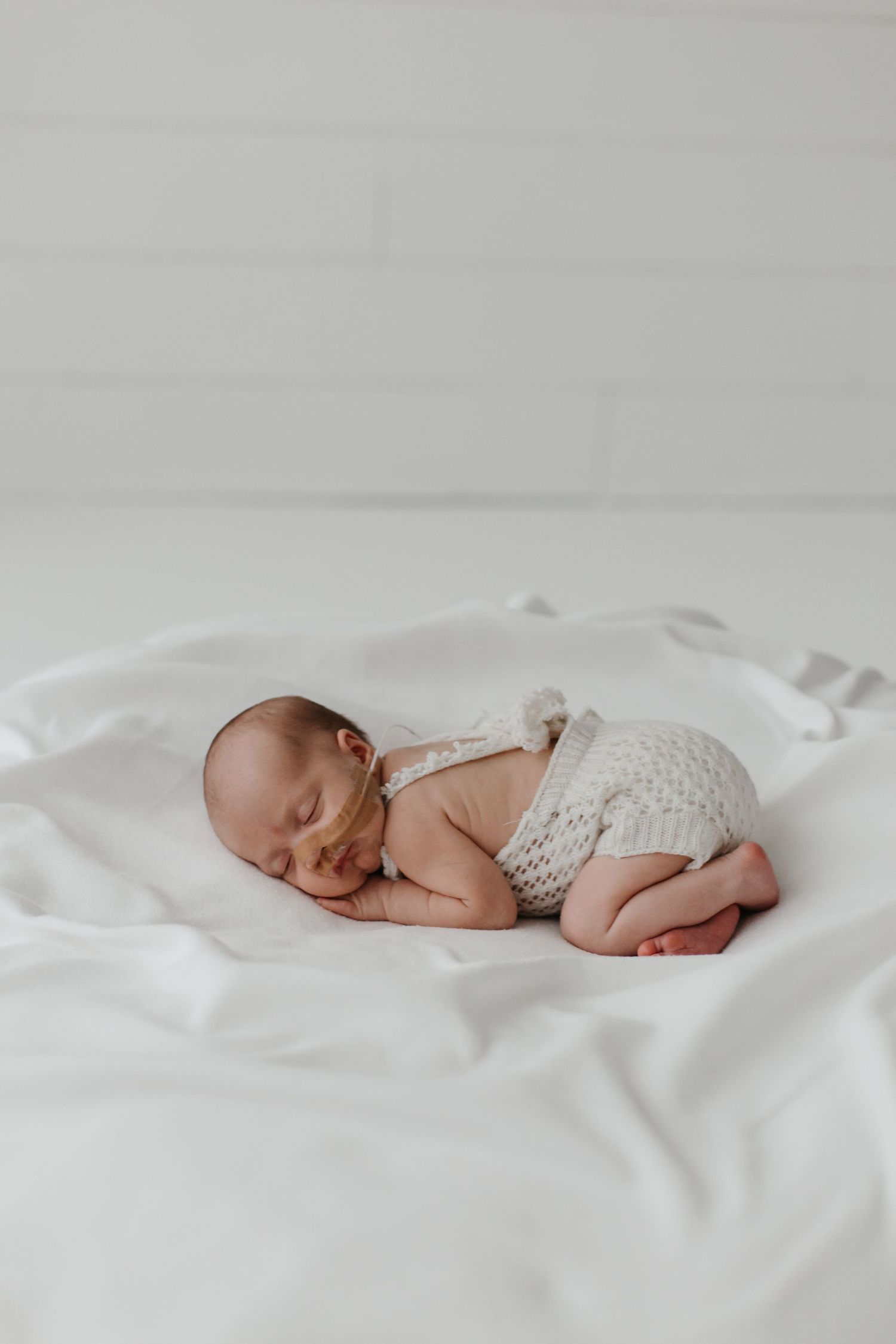 Sleeping newborn baby wearing knit outfit lies on soft white bedding.
