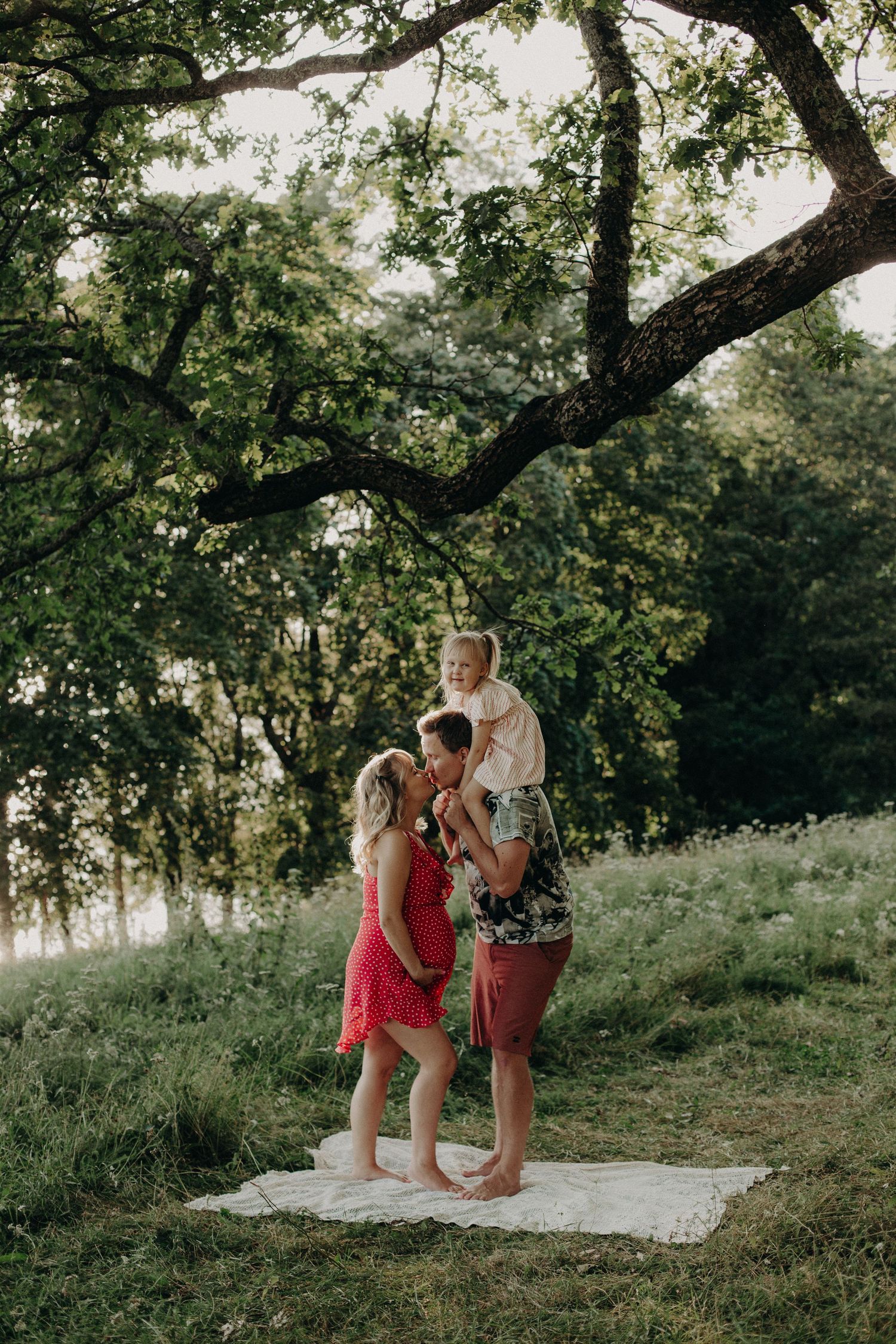 Sweet family moments photographed on a white blanket against a backdrop of trees and grass.
