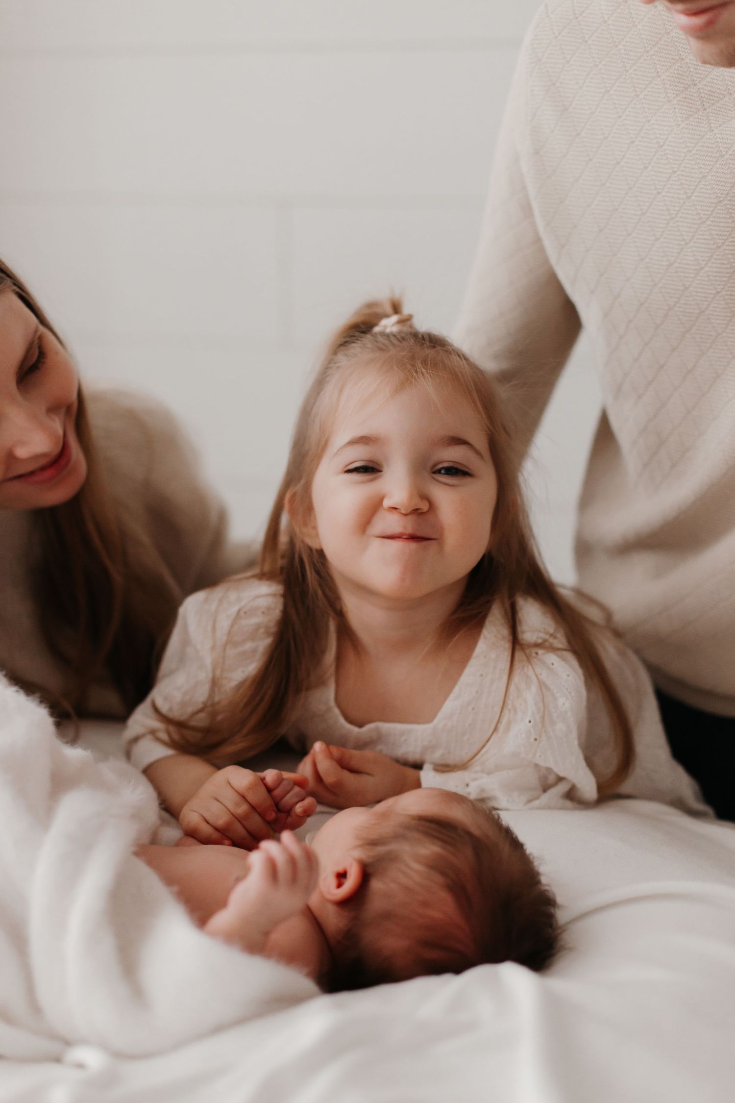 Family enjoying tender moments with newborn on white bedding.