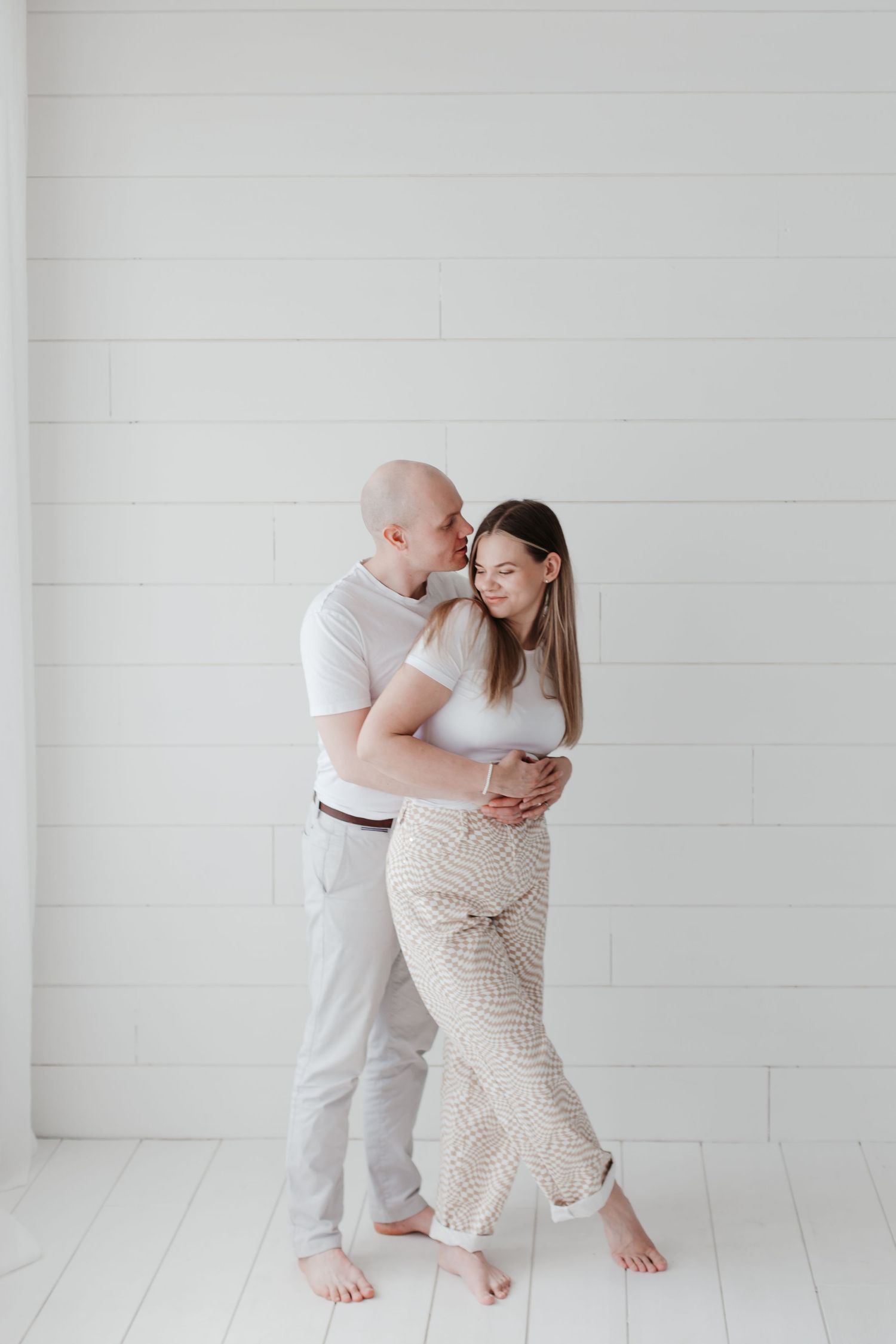 A couple dances together in a bright white room with wooden floors.