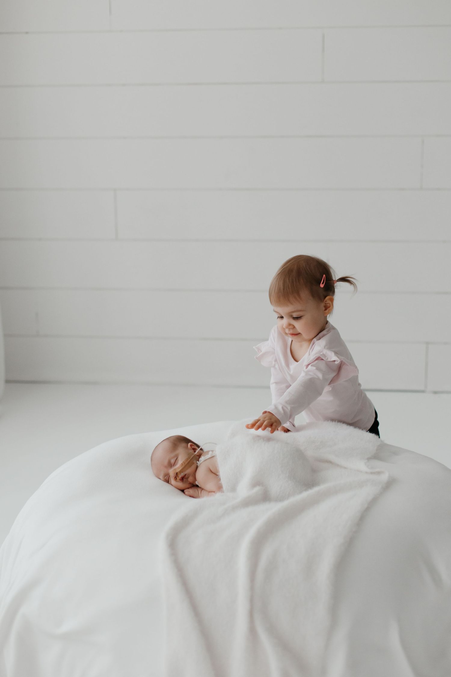 A toddler explores white bedding in a bright, clean room setting.