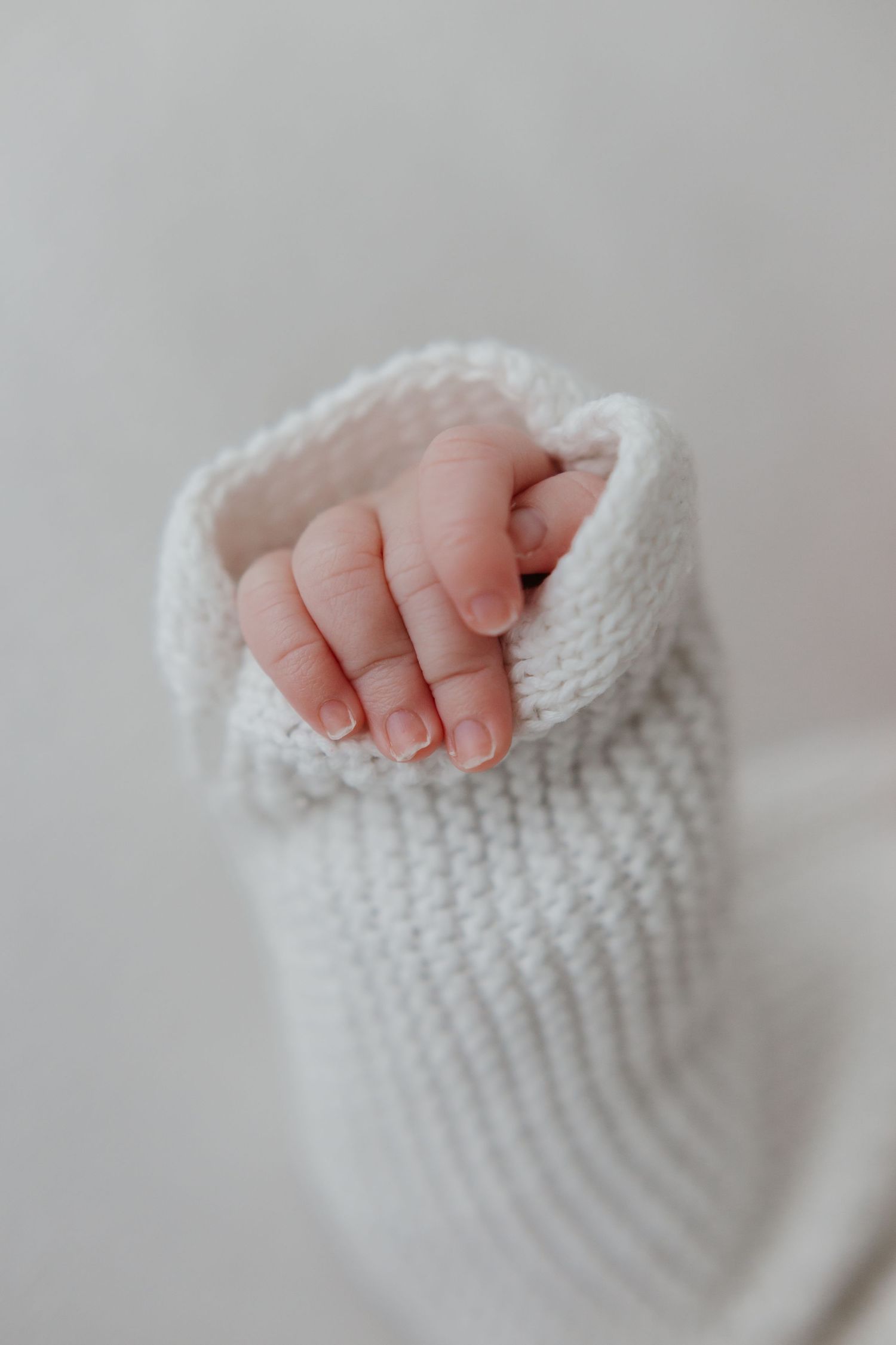 Close-up of tiny baby fingers resting on white knitted fabric.