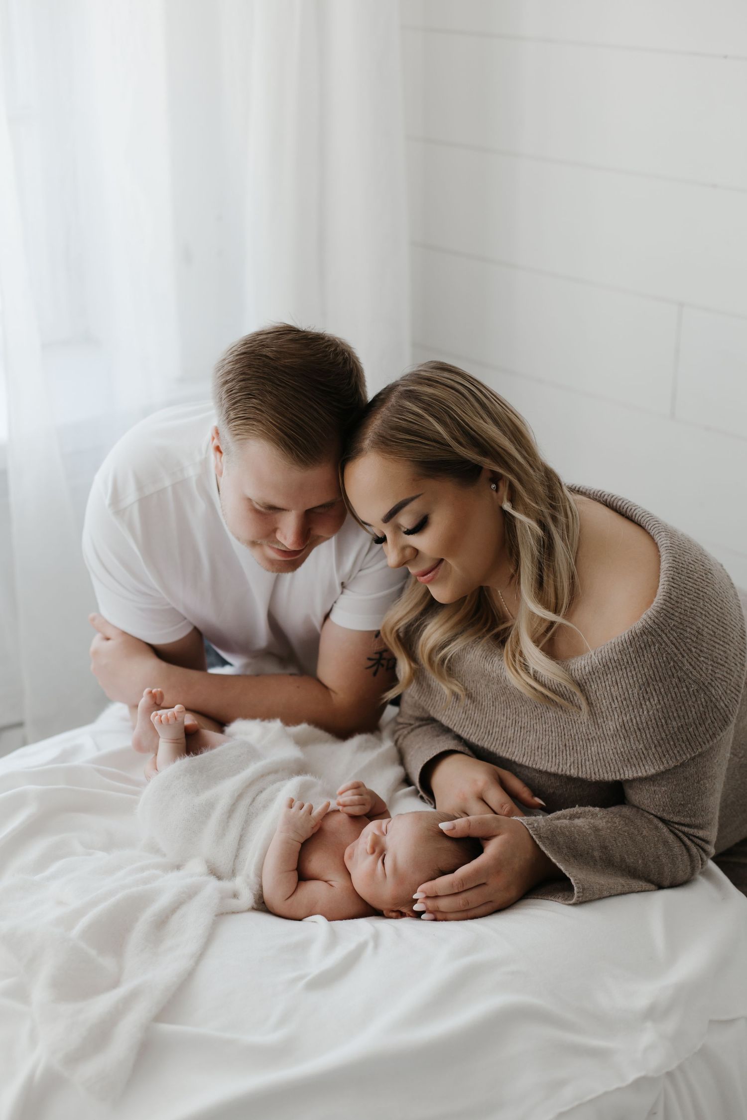 Family lying together on white bed sharing tender moment with newborn.