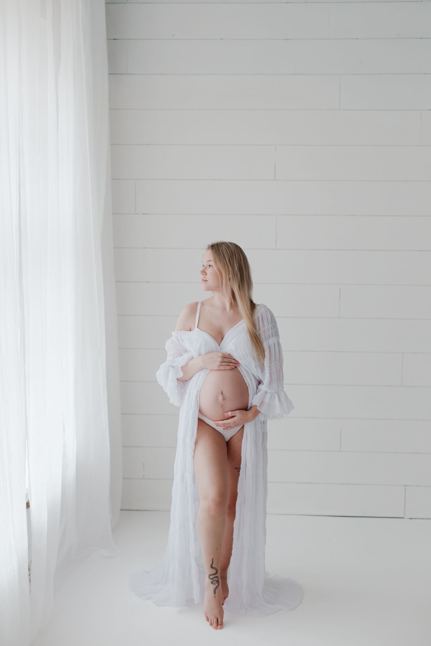 Artistic maternity portraits with sheer white robe in bright studio setting.