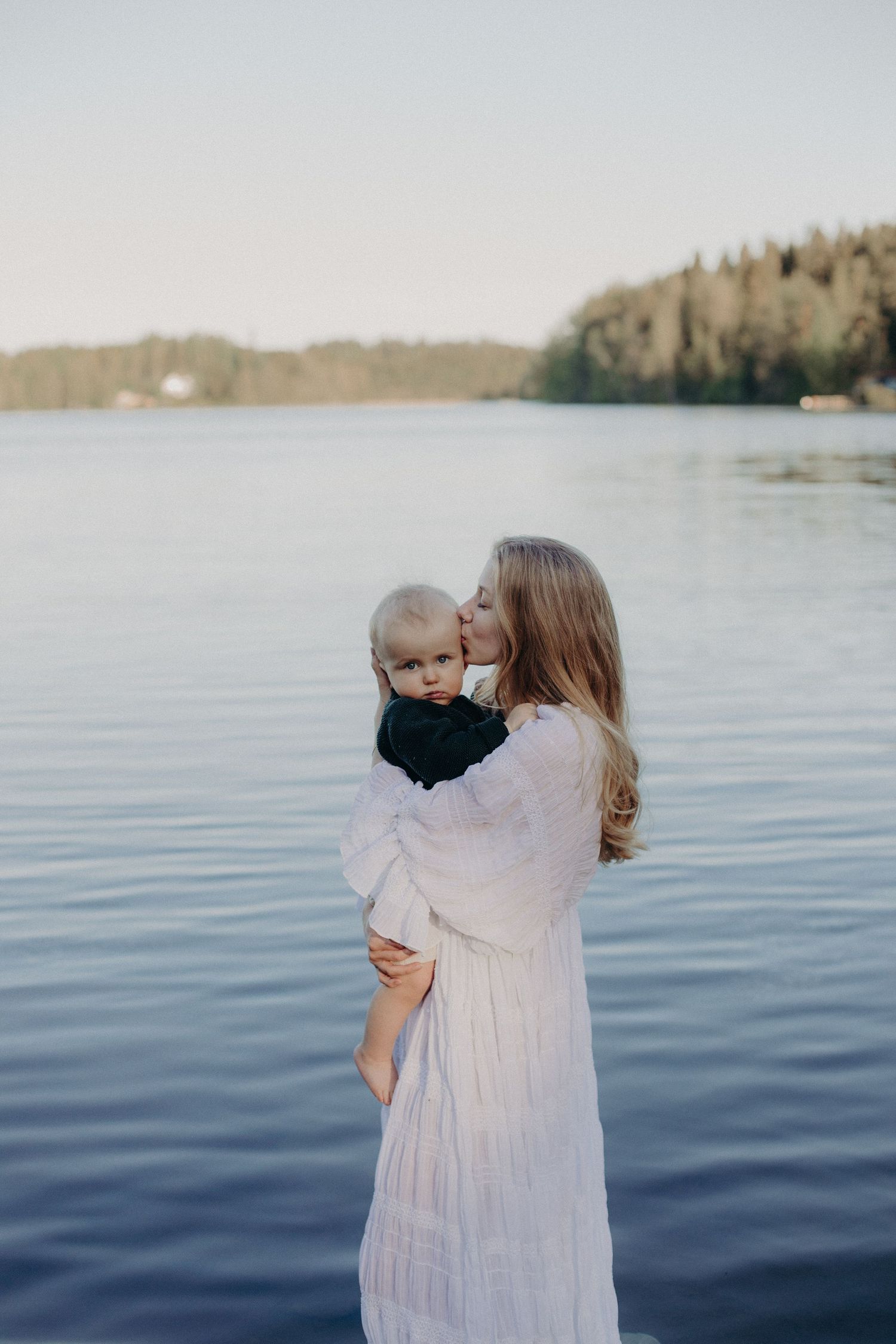 An intimate outdoor portrait against a peaceful lake backdrop with soft natural lighting.