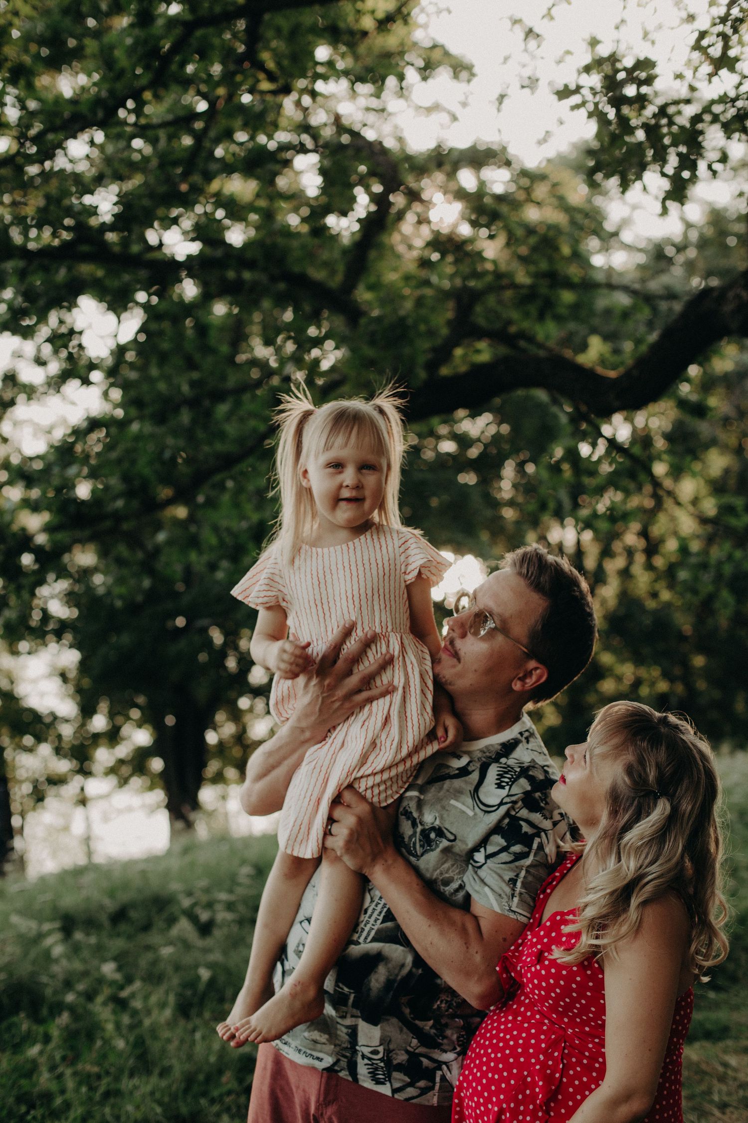 A joyful family moment captured outdoors during golden hour under tree branches.