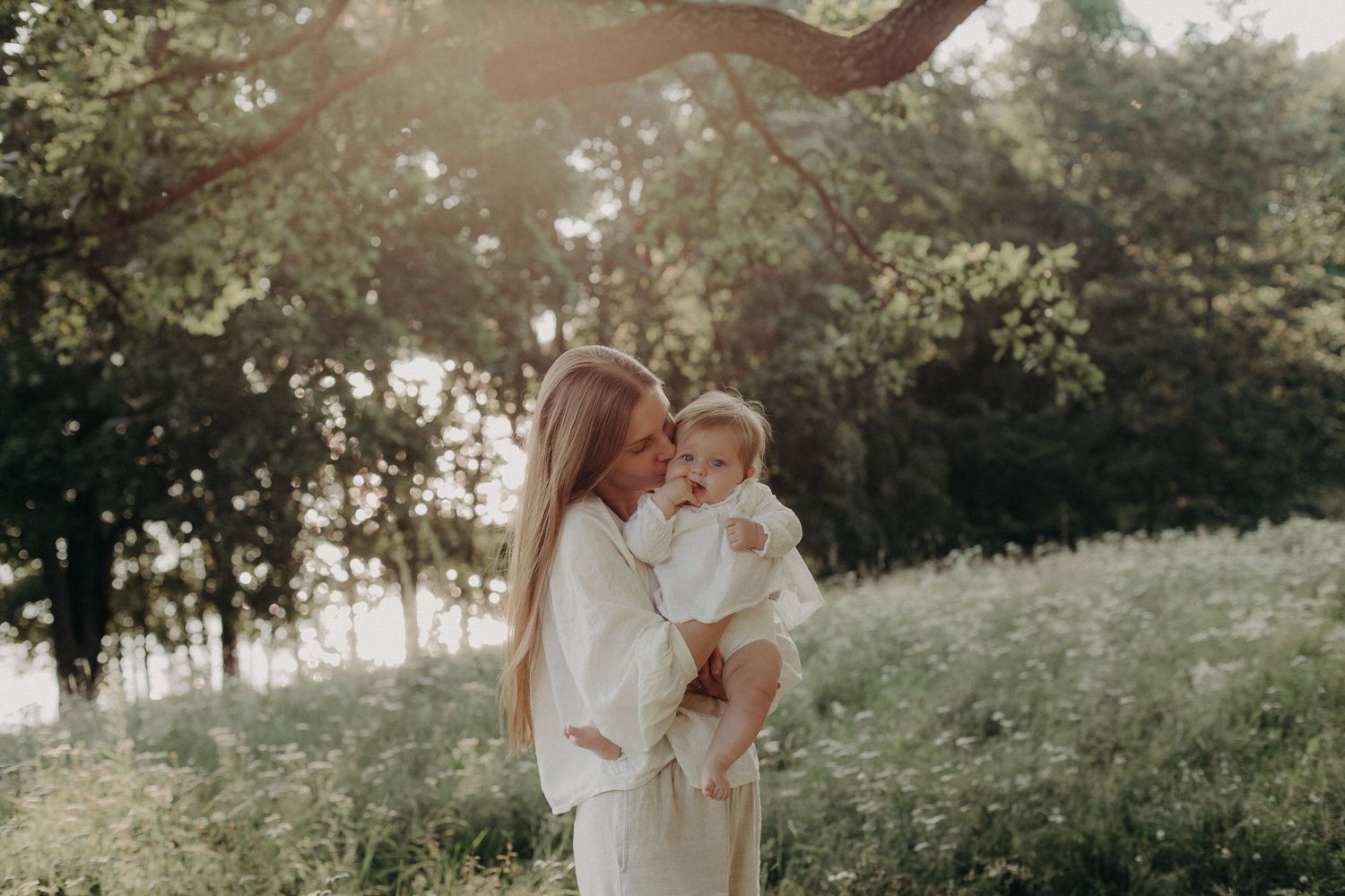 Mother and child share tender moment in dreamy outdoor setting at sunset.