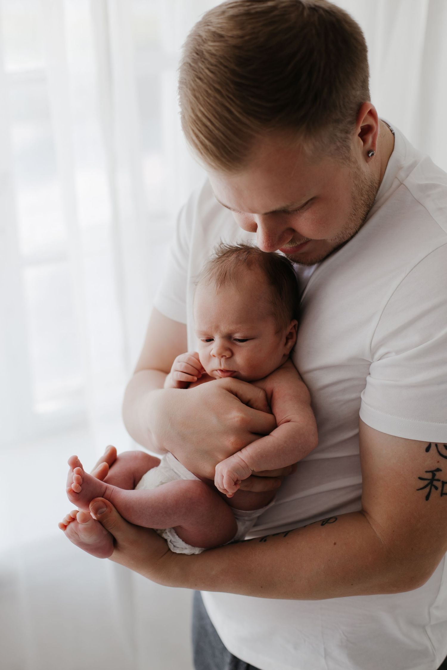 Parent in white shirt tenderly holds and kisses newborn baby in intimate portrait series.