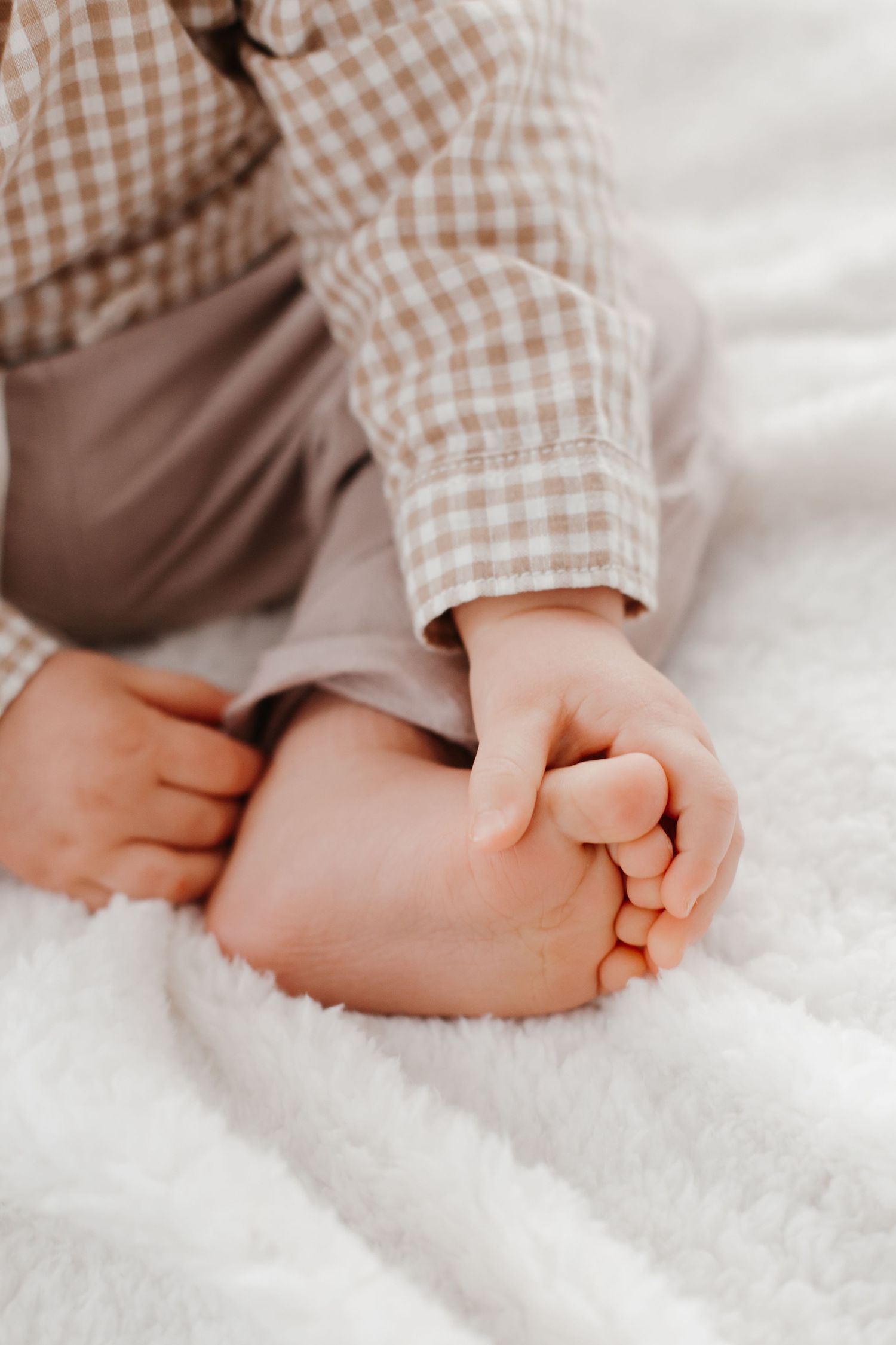 Close-up of baby feet and hands on soft white textured blanket.