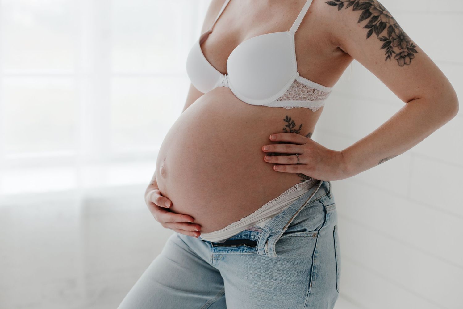 Close-up shots of pregnant belly with floral tattoo visible in white studio setting.