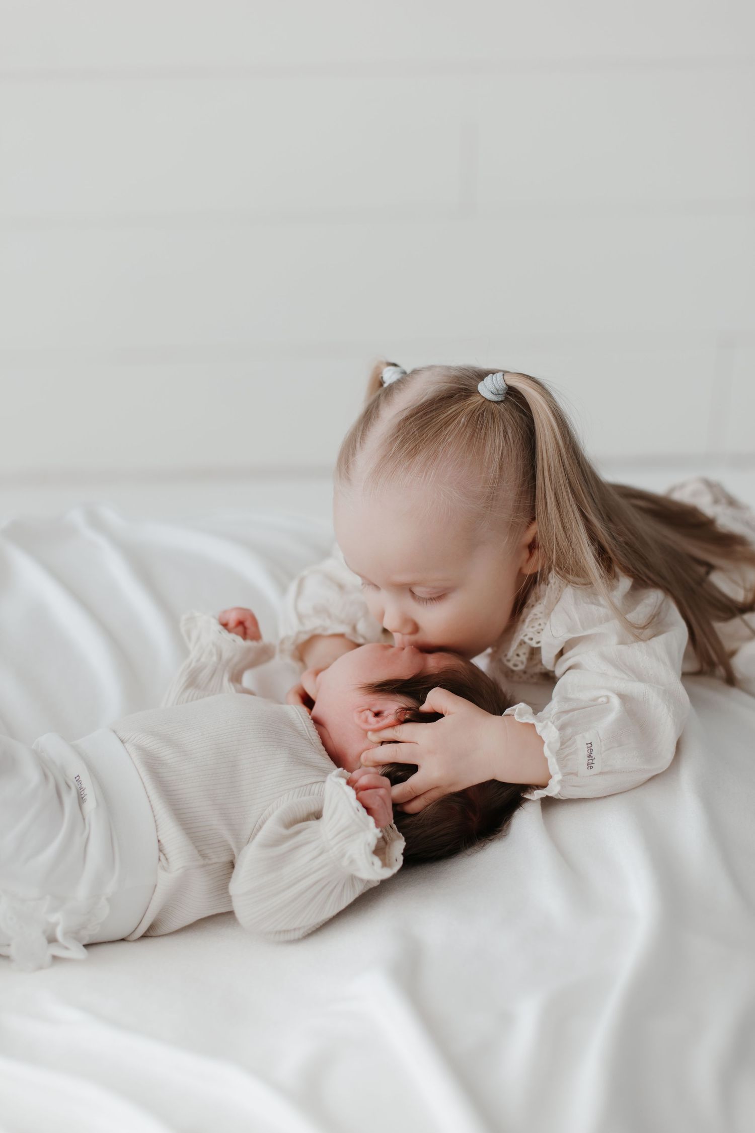 Small child in white ruffled dress lying on soft white bedding.