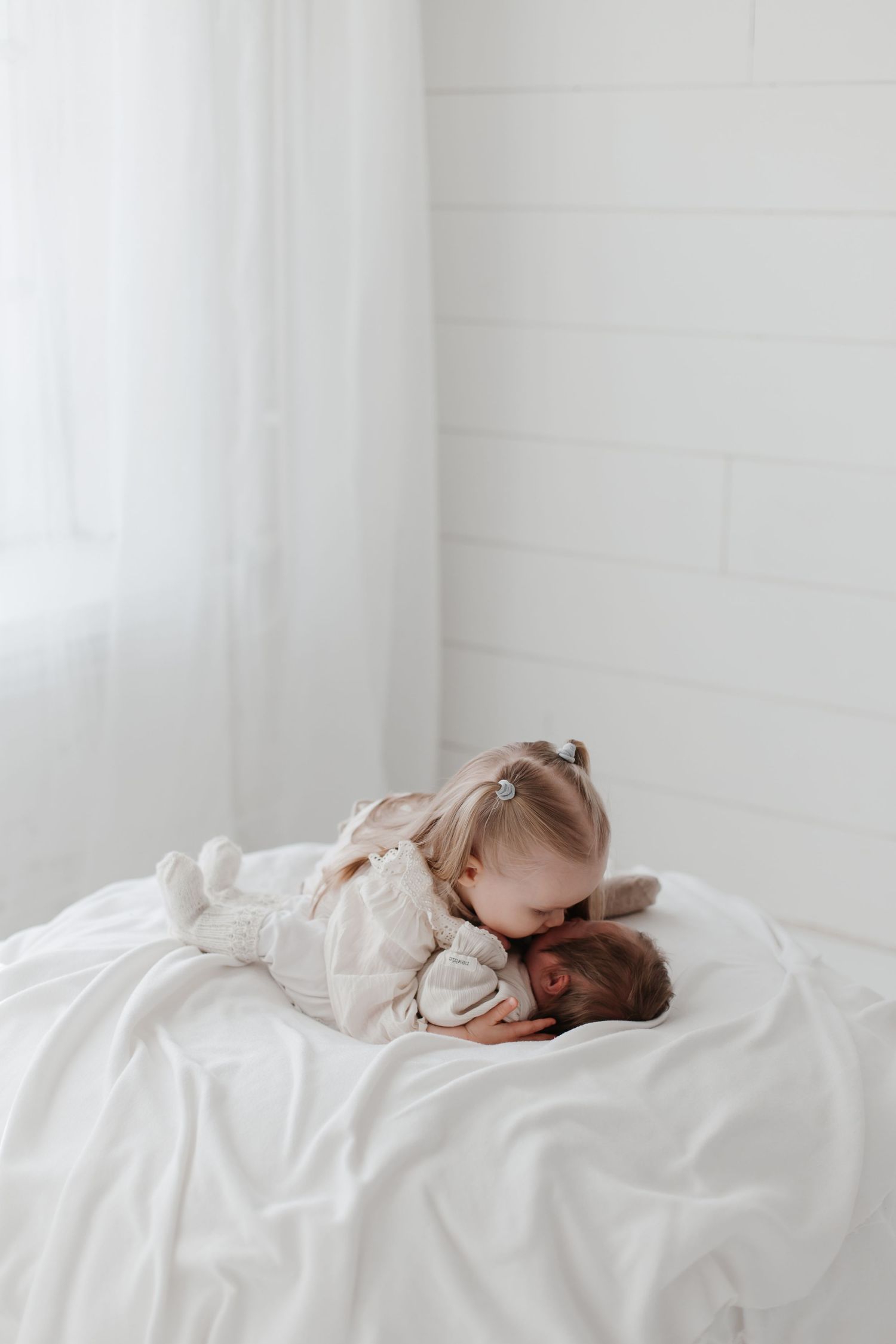Baby resting peacefully on white sheets in a bright minimalist setting.