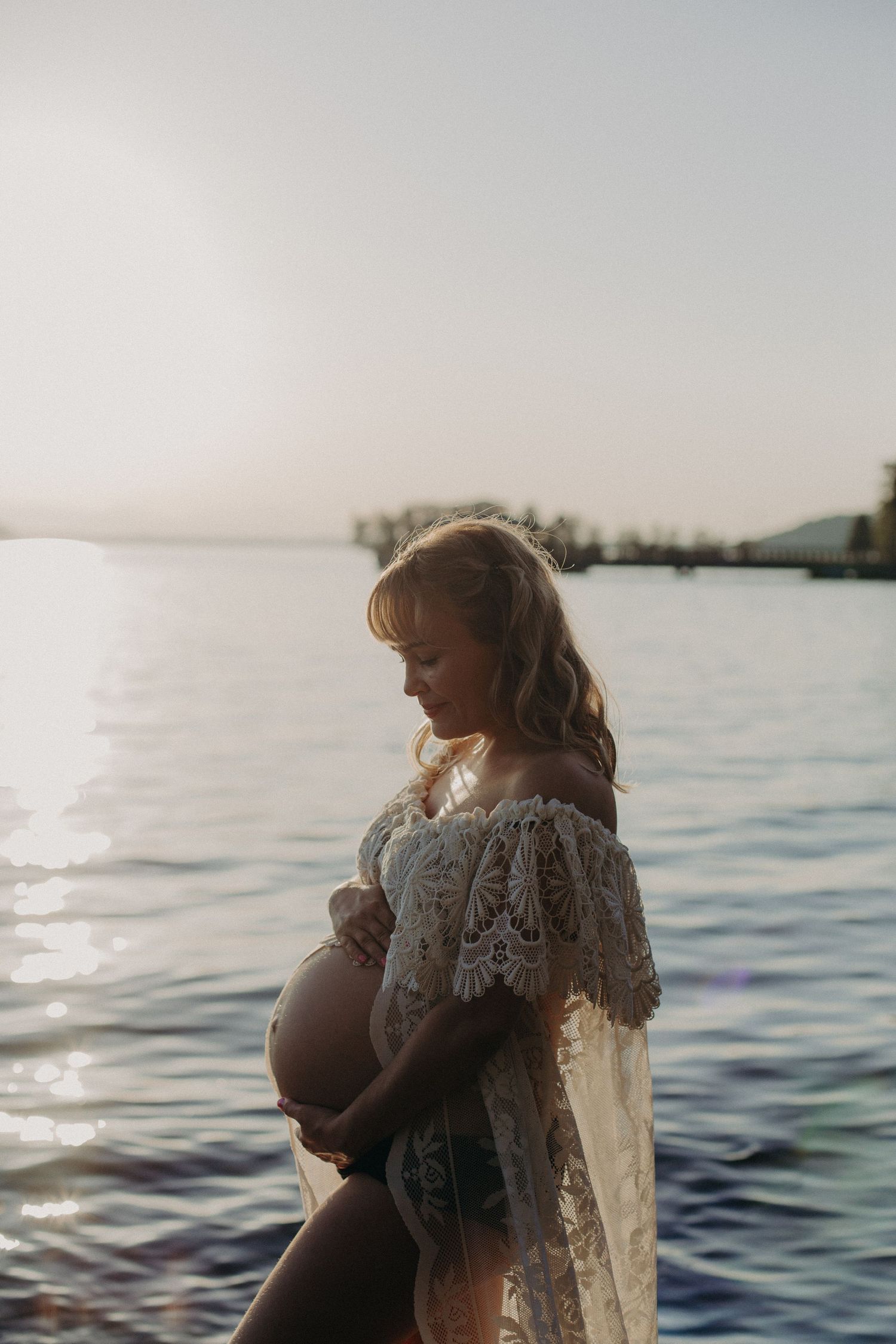 Intimate lakeside maternity moment captured in warm evening light.