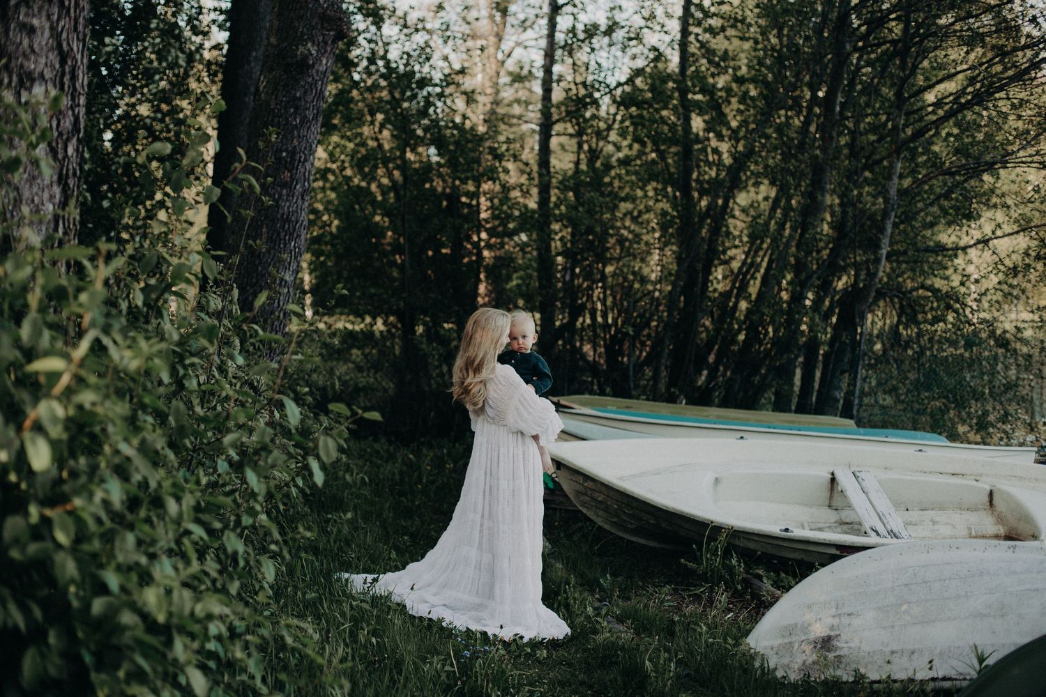 Maternity photos in outdoor garden setting with flowing white dress and natural scenery.