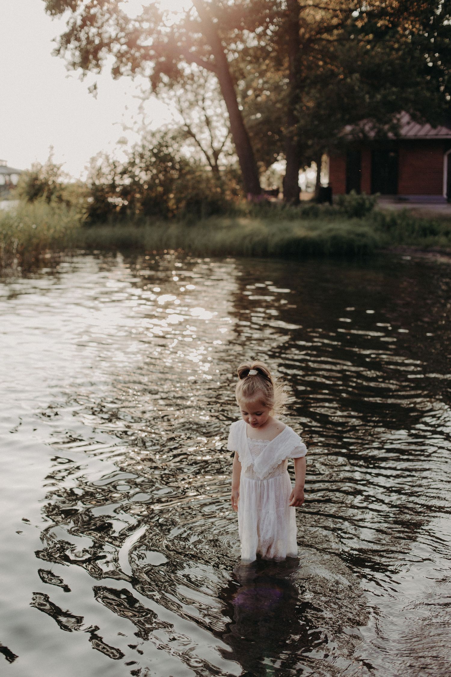 A figure in white explores the shallow waters of a lake at sunset.
