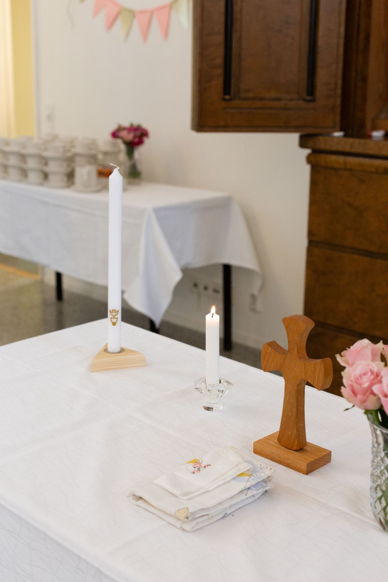 White table setting with pink flowers, candles and wooden cross for baptism or communion.