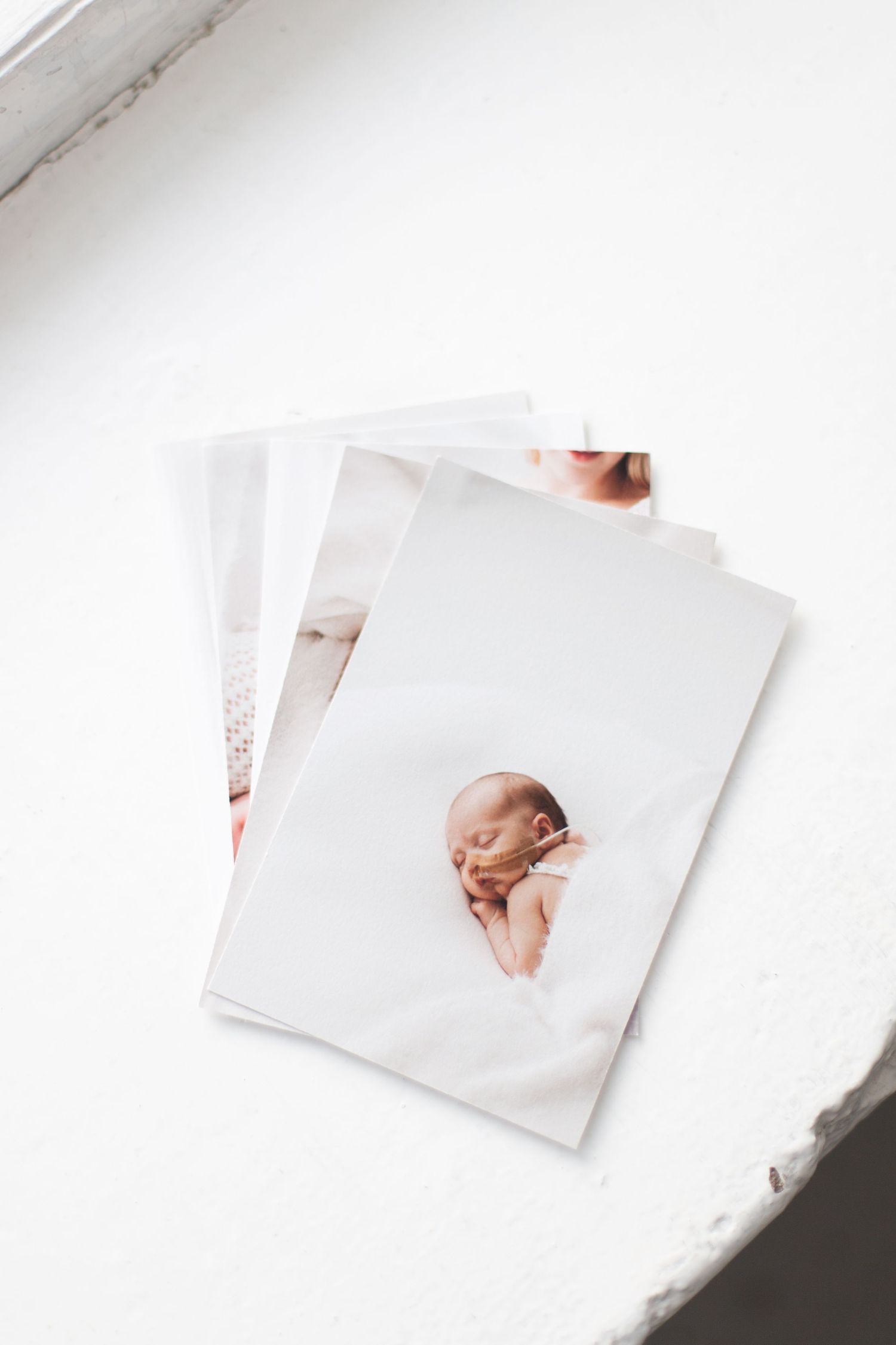 A stack of white photographs featuring a newborn baby portrait against a bright white background.
