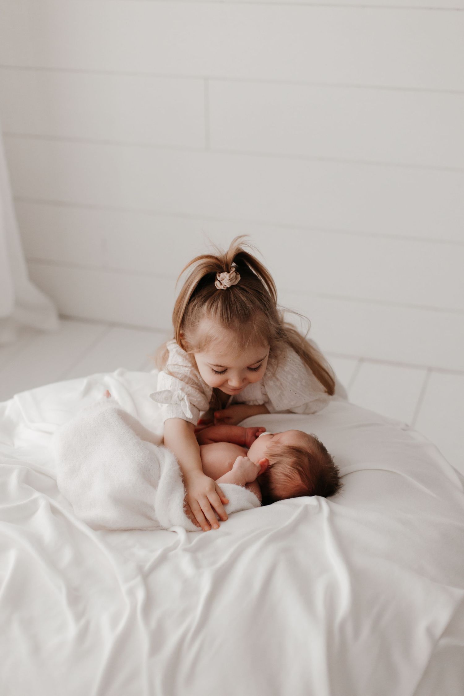 Siblings sharing sweet moment together on white bedding.