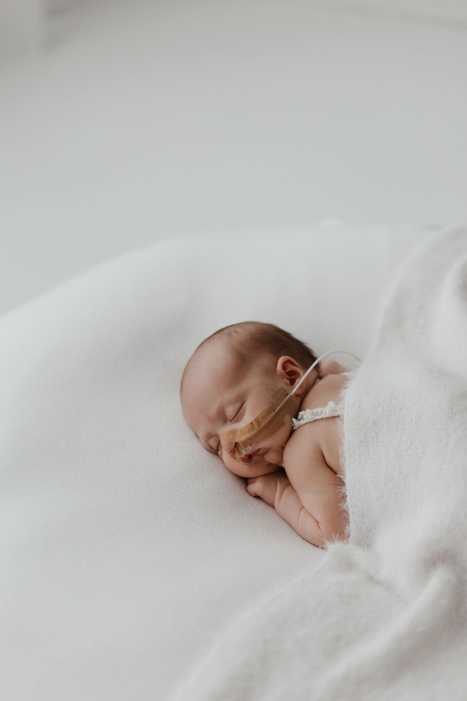 A sleeping newborn wrapped in white blankets on a soft white background.