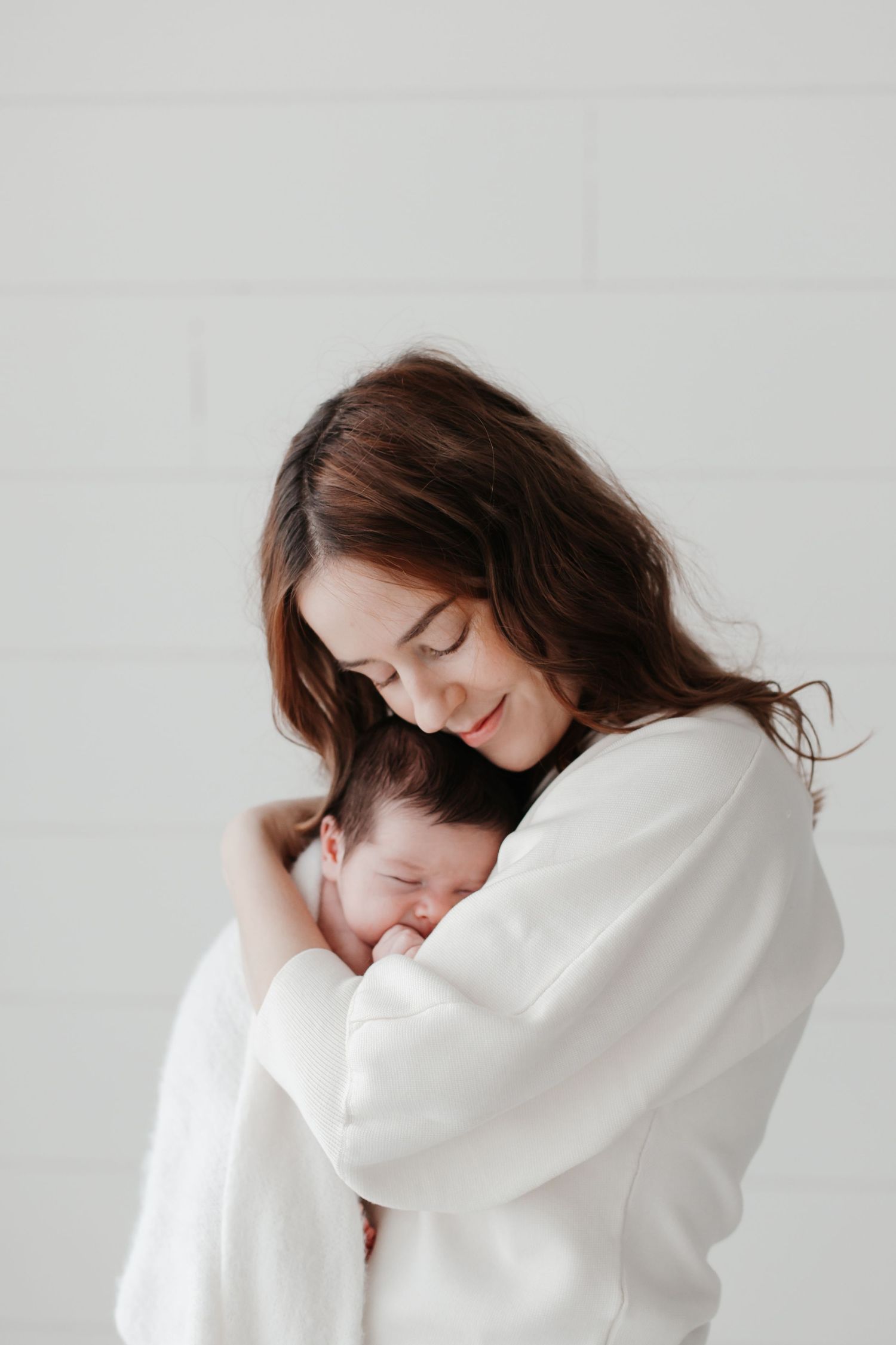 Parent in white sweater cuddles sleeping newborn with tender smile.
