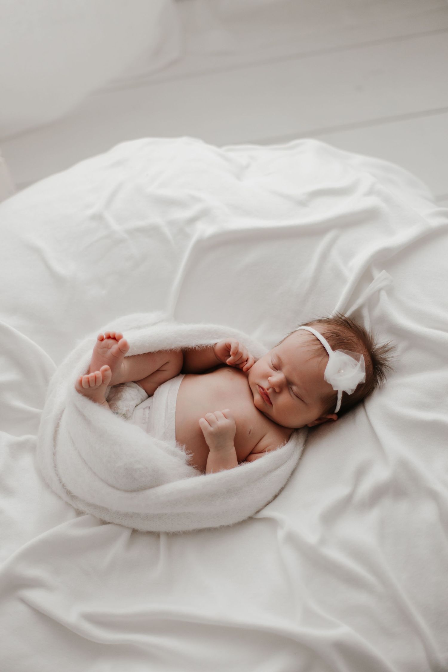 Newborn baby sleeping on white bedding in minimalist setting.