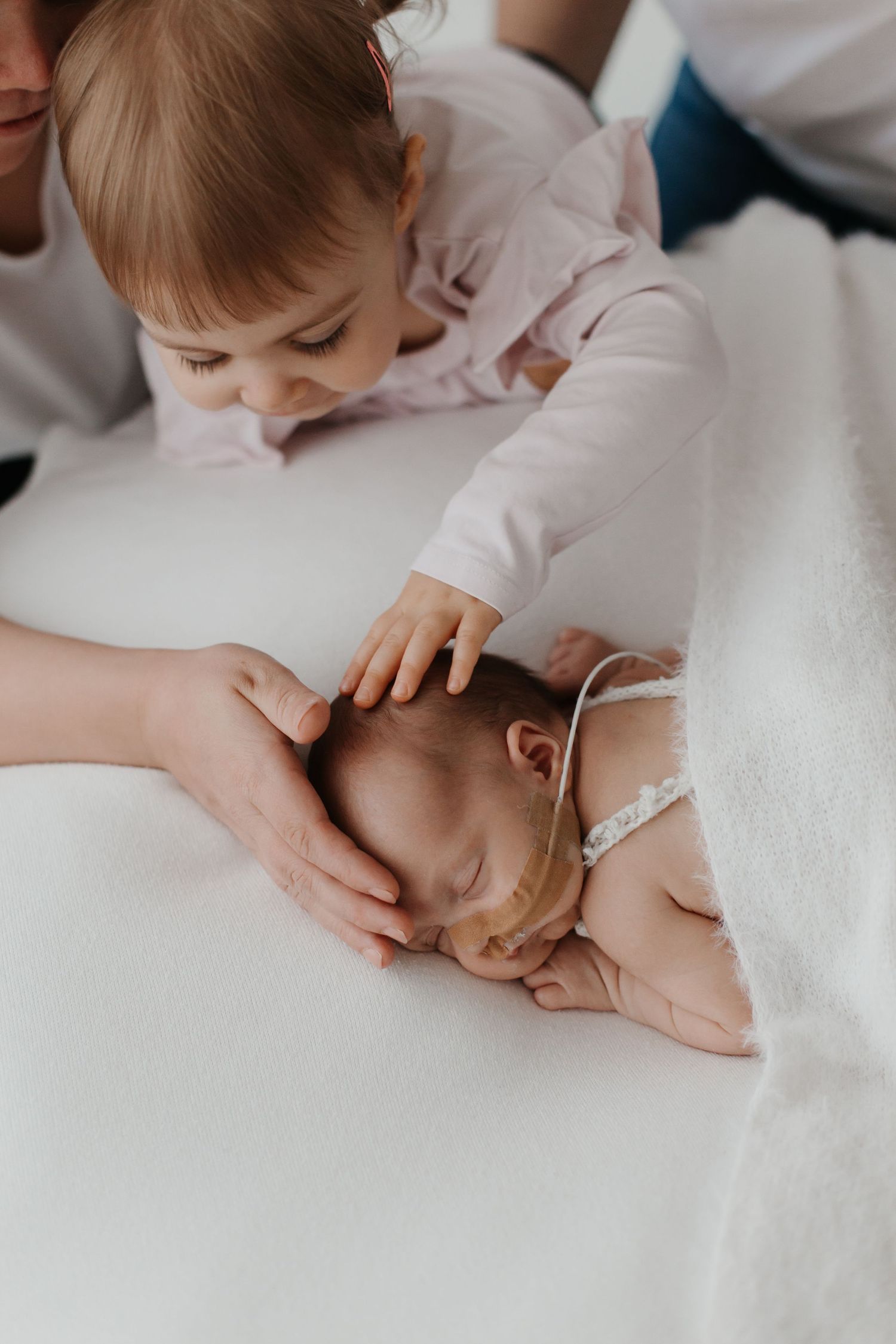 Family members share tender moments on white bedding during a photo shoot.