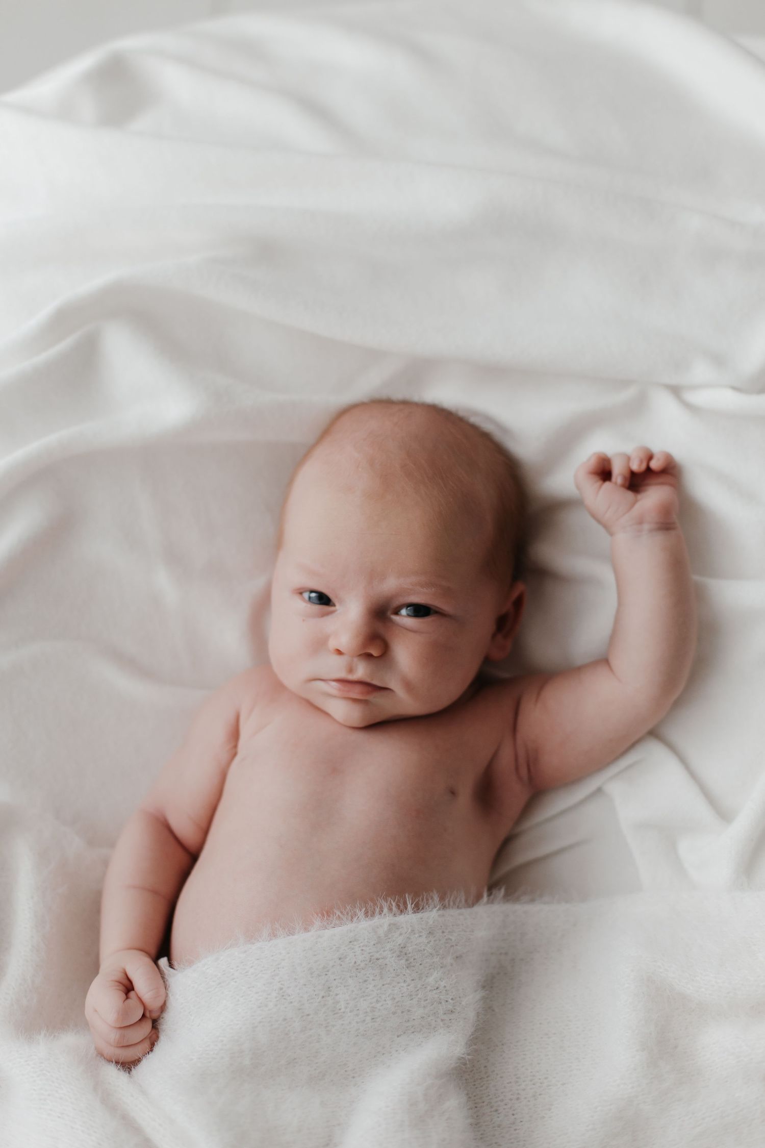 Newborn baby lying on soft white bedding in natural light.