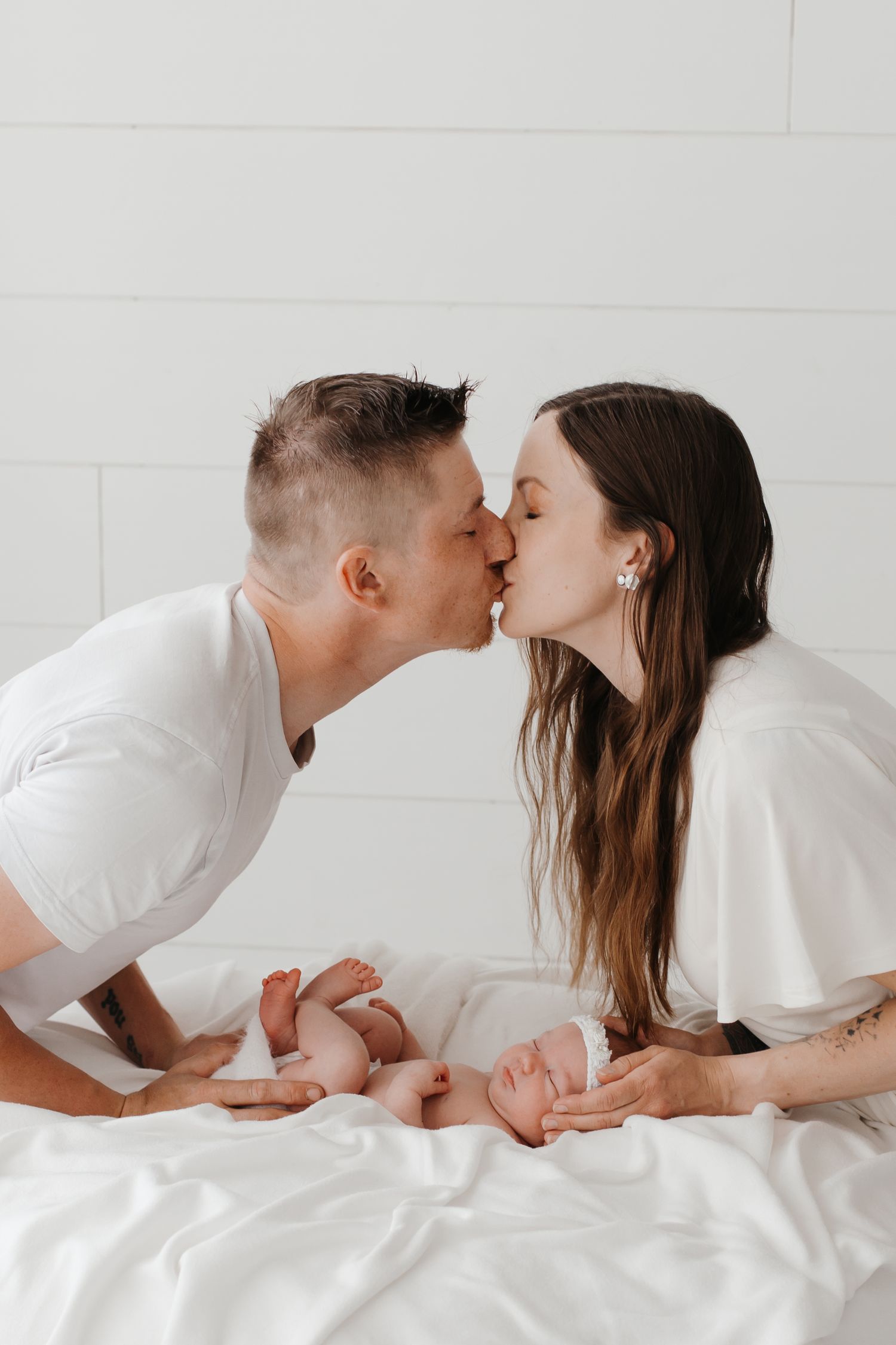 Couple sharing intimate moment on white bedding during photo session.