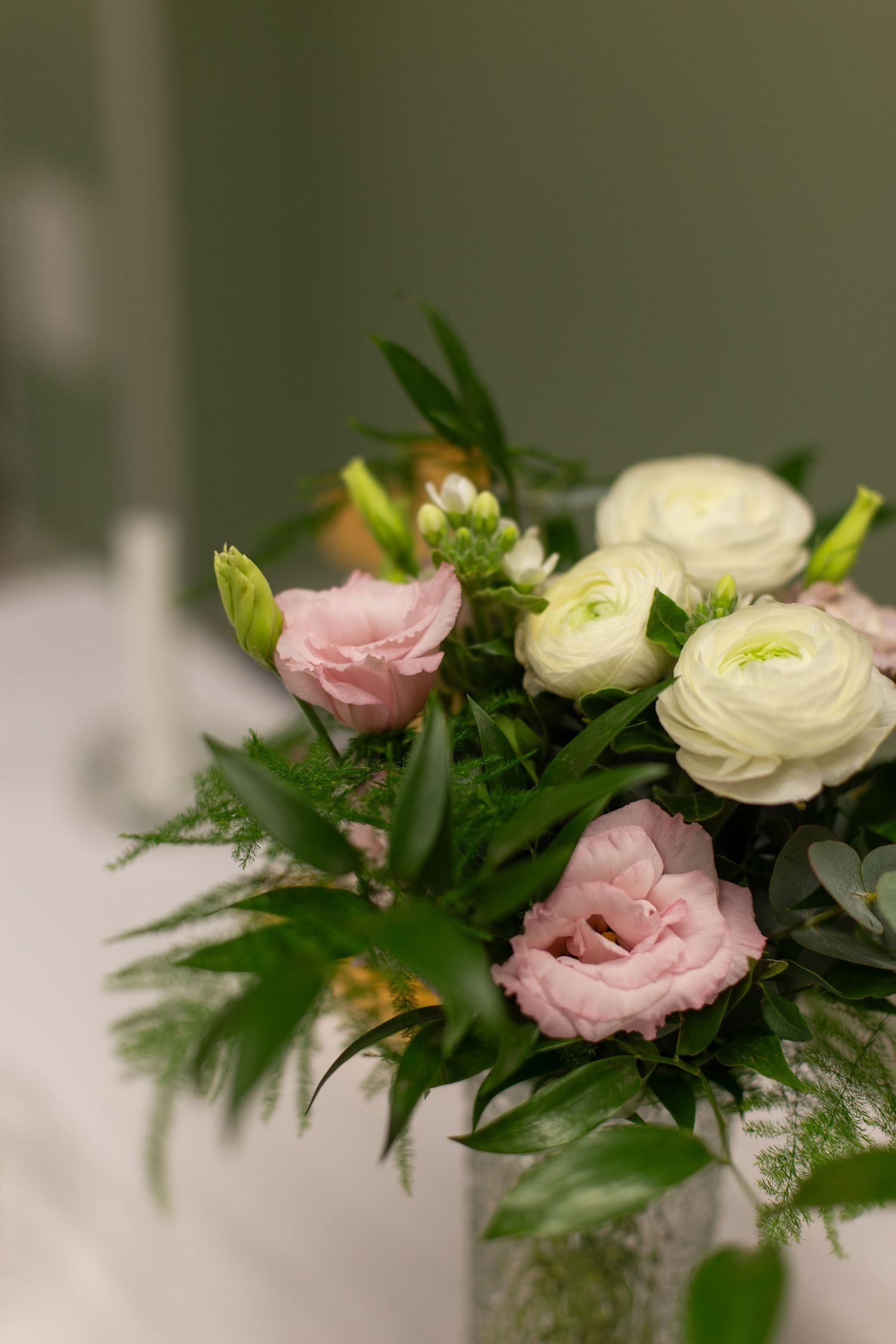 Elegant bouquet of pink lisianthus and white ranunculus flowers with lush green foliage in a vase.