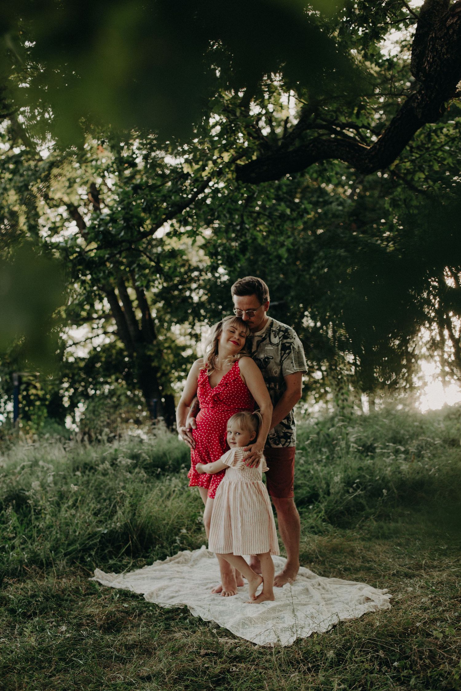 Sweet outdoor photoshoot scene with a white blanket spread on grassy ground under dappled sunlight.