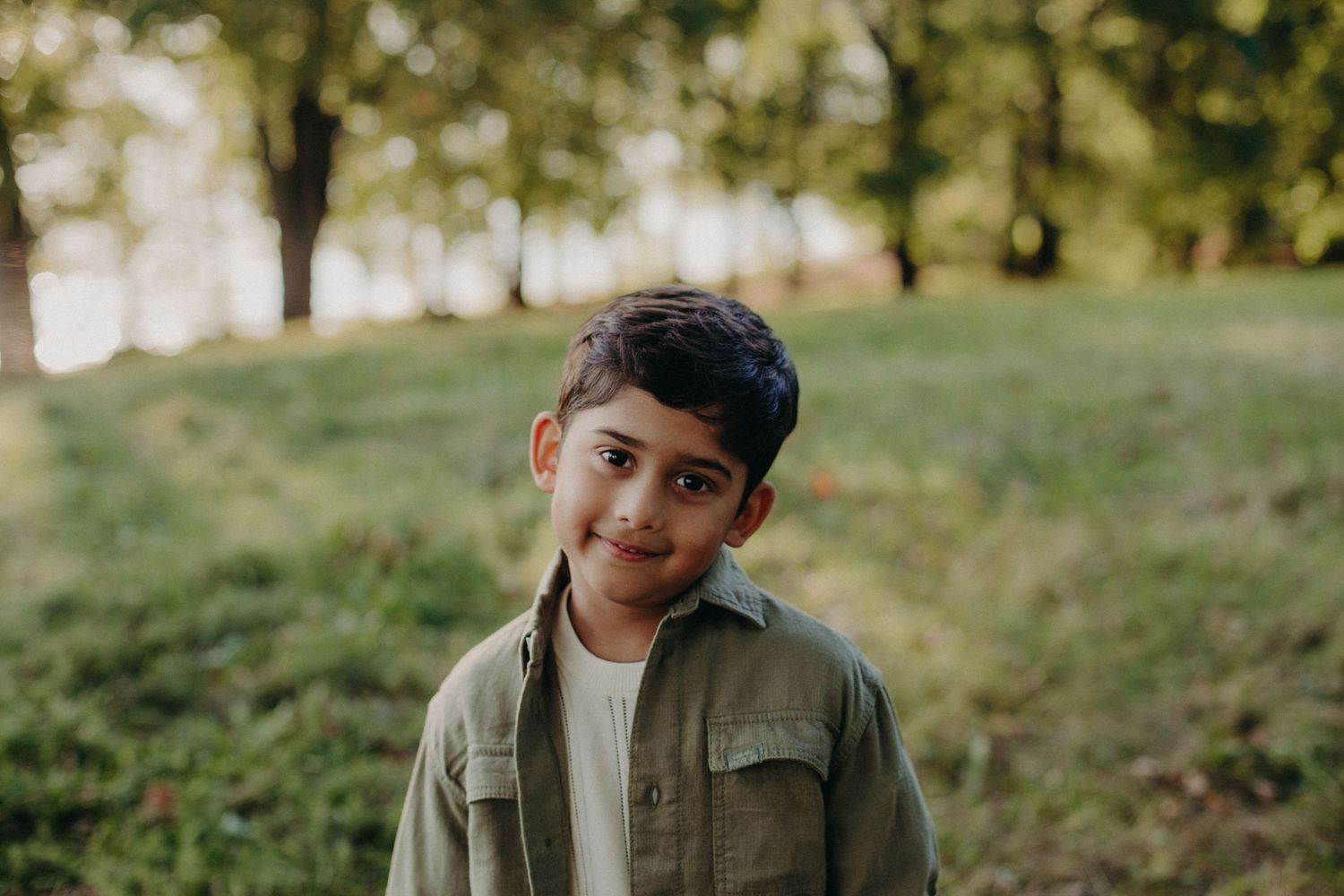 Candid outdoor portrait in a sunlit park with green trees in background.