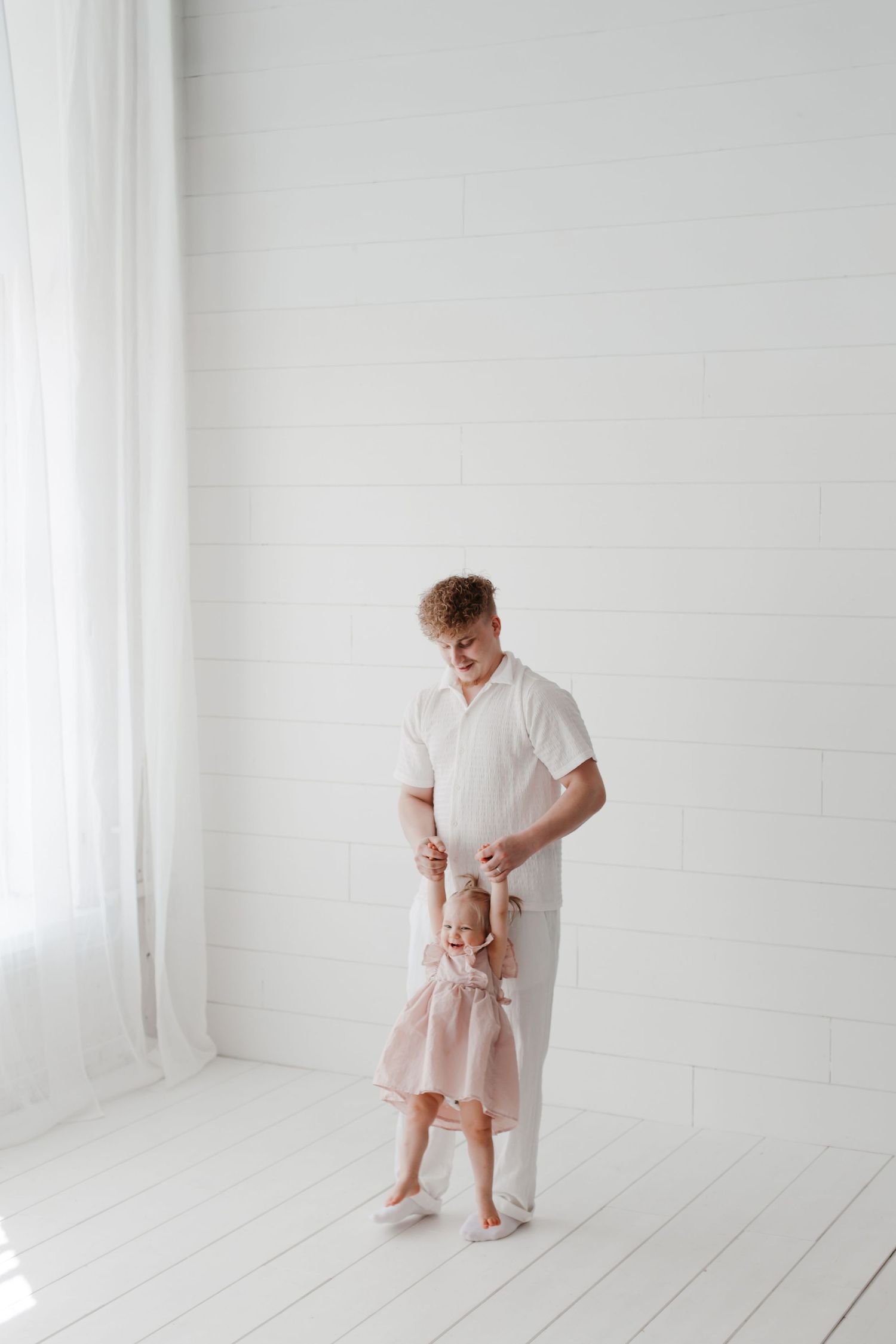 A tender moment captured in a bright white studio as a toddler practices walking.