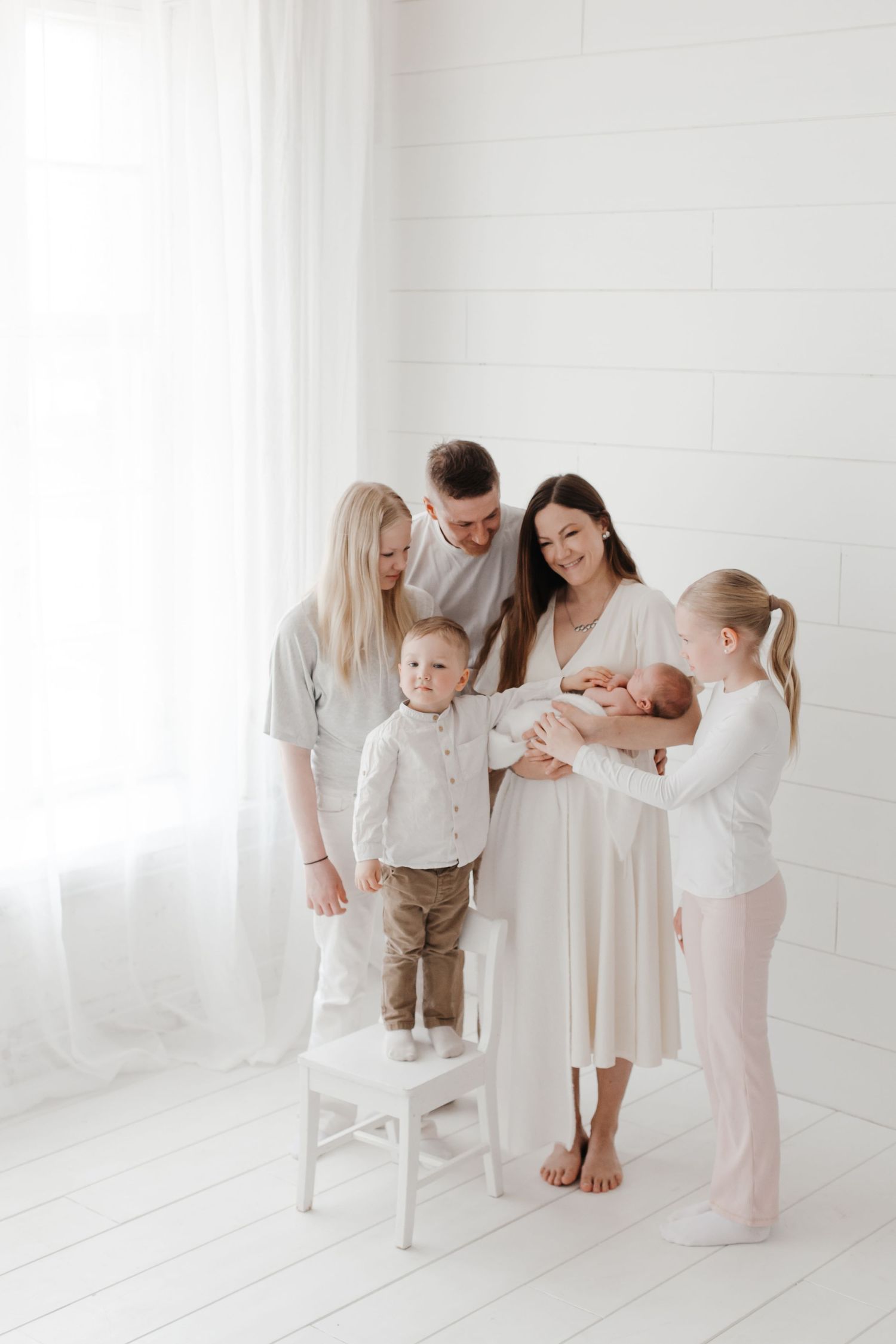 Family members interacting with a newborn baby in an all-white studio setting.