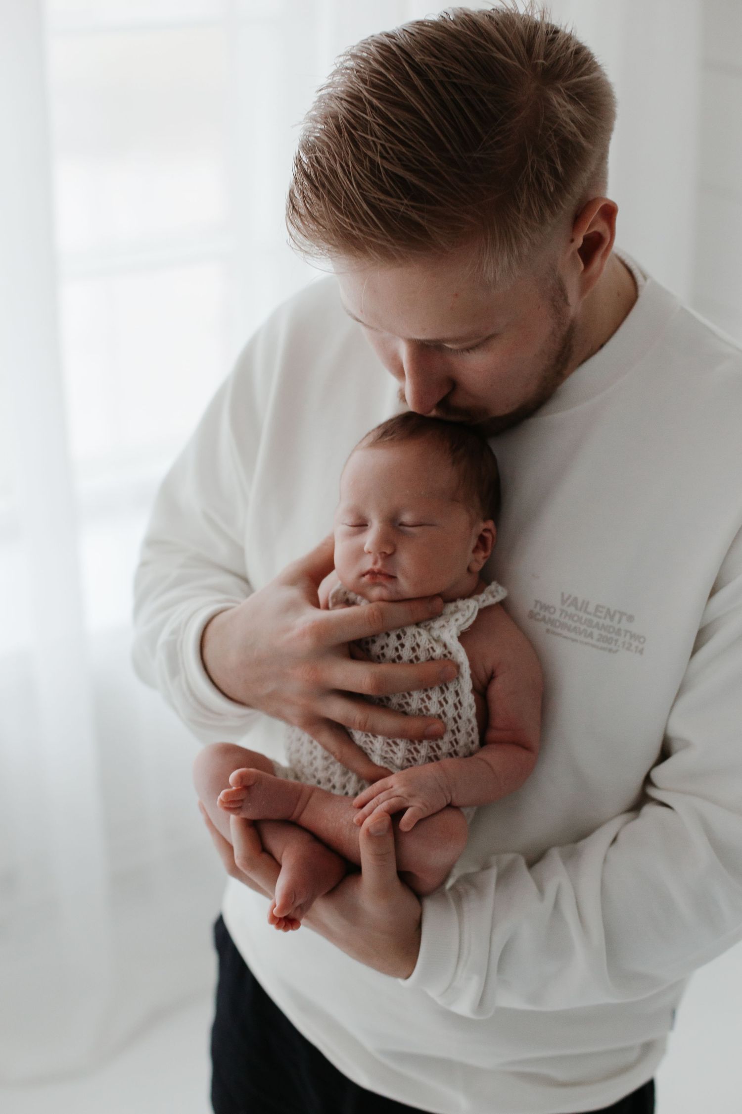 Parent in white sweater holding sleeping newborn close to chest.