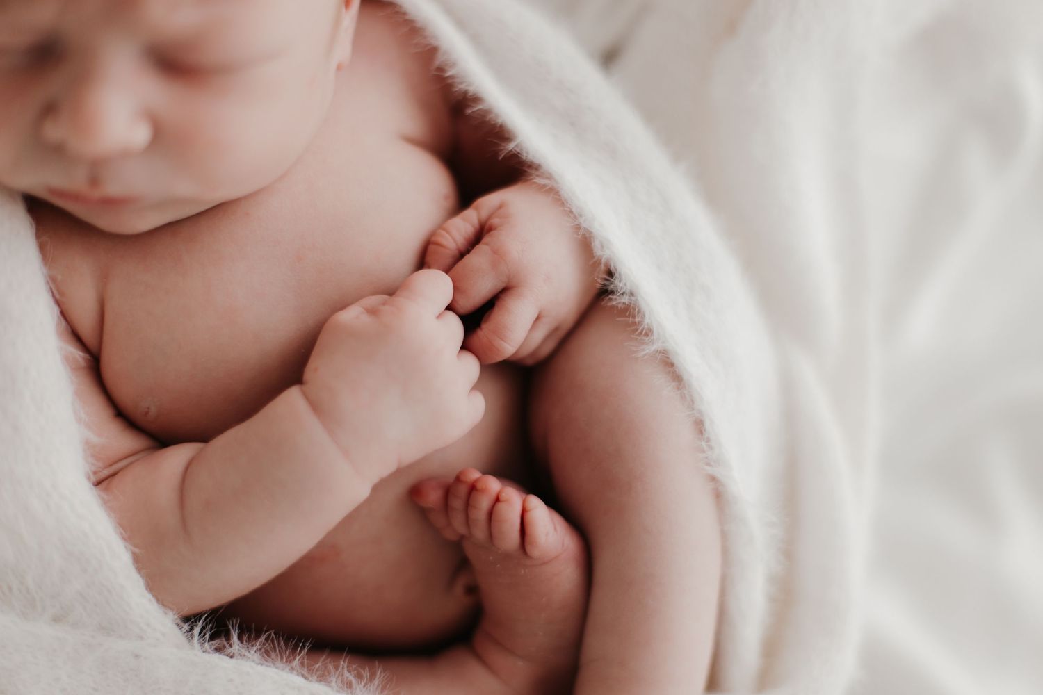 Close-up of newborn baby's tiny fingers and toes on white bedding.