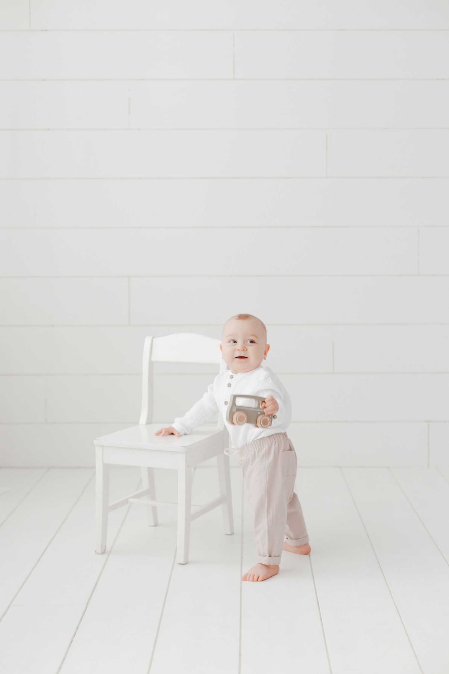 Infant practicing standing while holding onto white wooden chair.