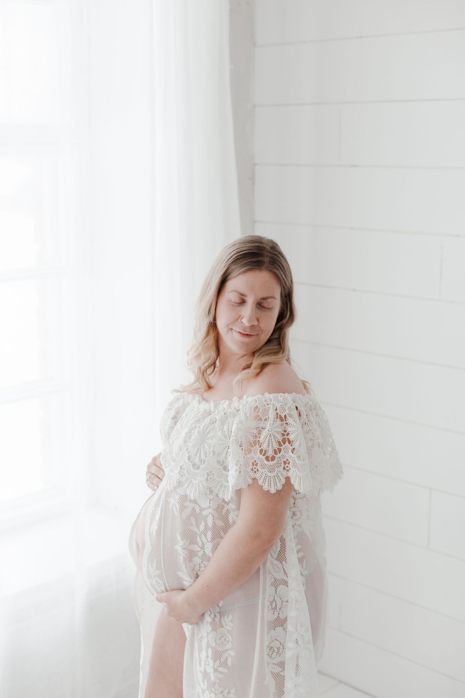 Minimalist maternity portrait against white shiplap wall with off-shoulder lace dress.