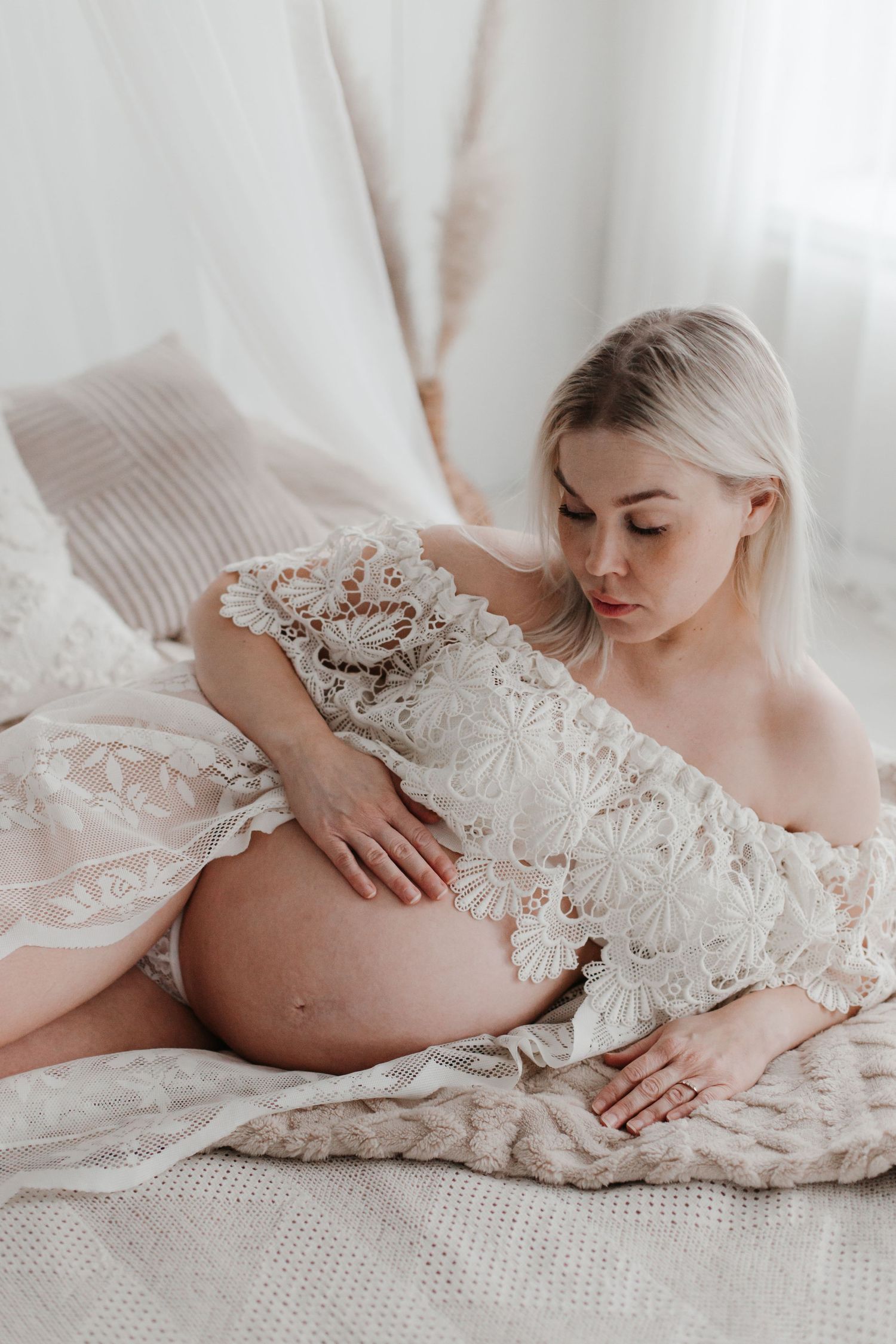 Artistic maternity portrait featuring delicate lace dress and soft window lighting.