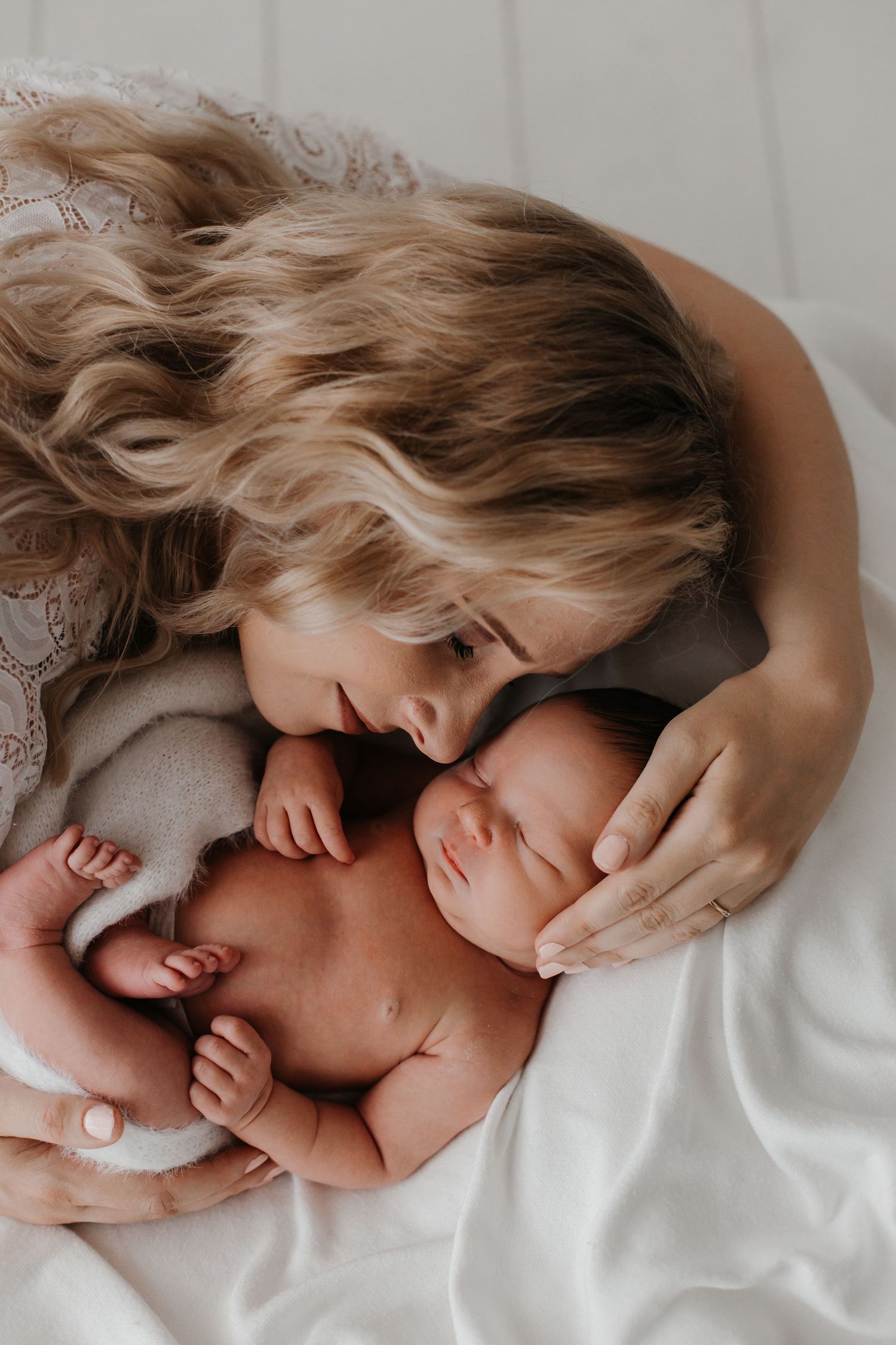 Mother and newborn sharing intimate bonding moment on white bedding.