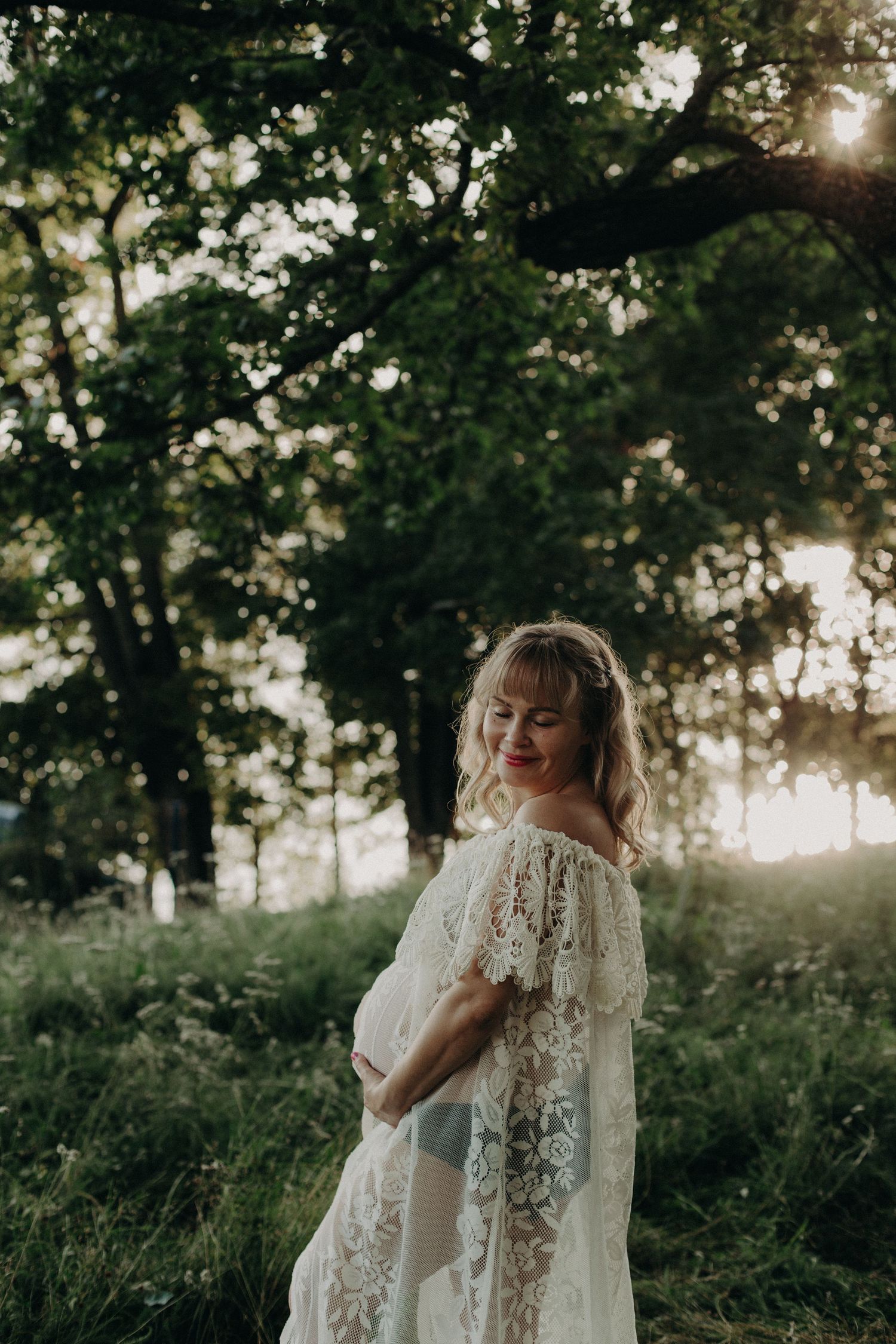 Dreamy woodland maternity session with flowing white lace dress at golden hour.