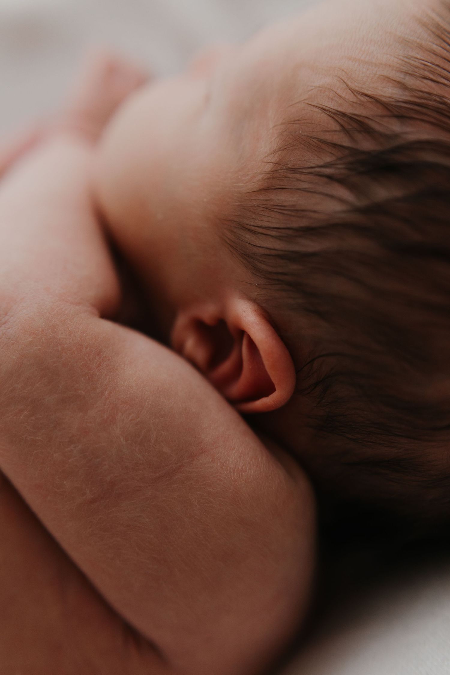 Peaceful sleeping newborn captured in intimate detail against soft white bedding.