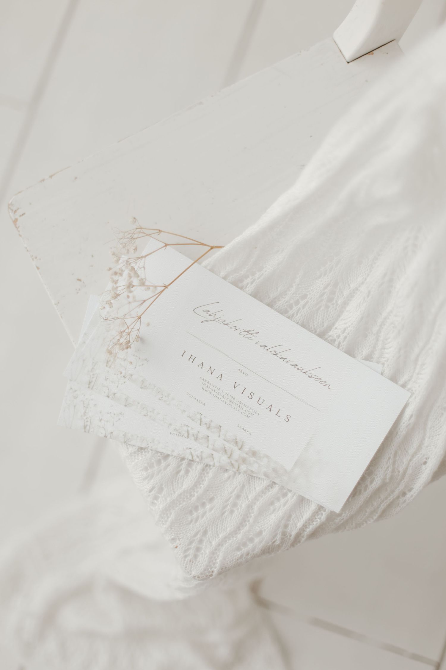 Elegant white business card with delicate text lying on soft white fabric.