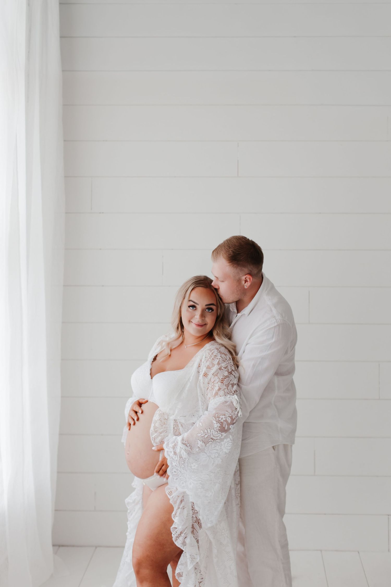 Sweet maternity moment captured in bright white studio setting.