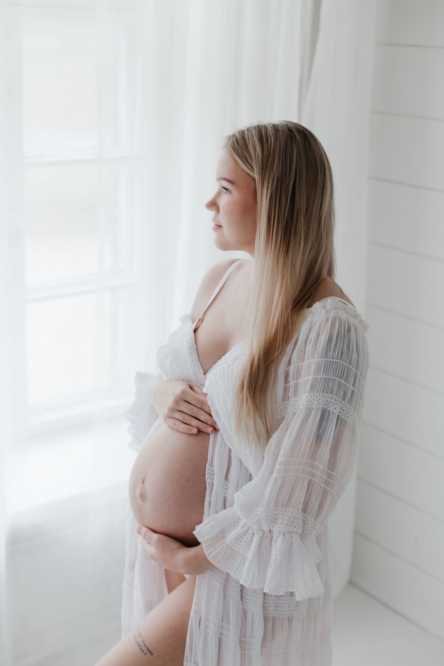 Dreamy maternity photos with flowing white lace robe in natural light studio.