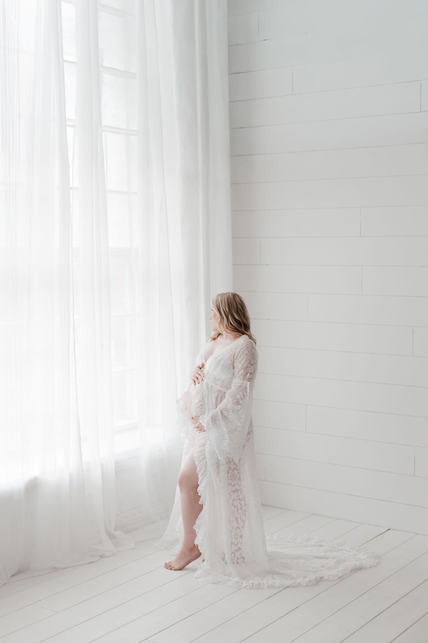 Ethereal white lace maternity photoshoot in a bright minimalist room with soft natural lighting.